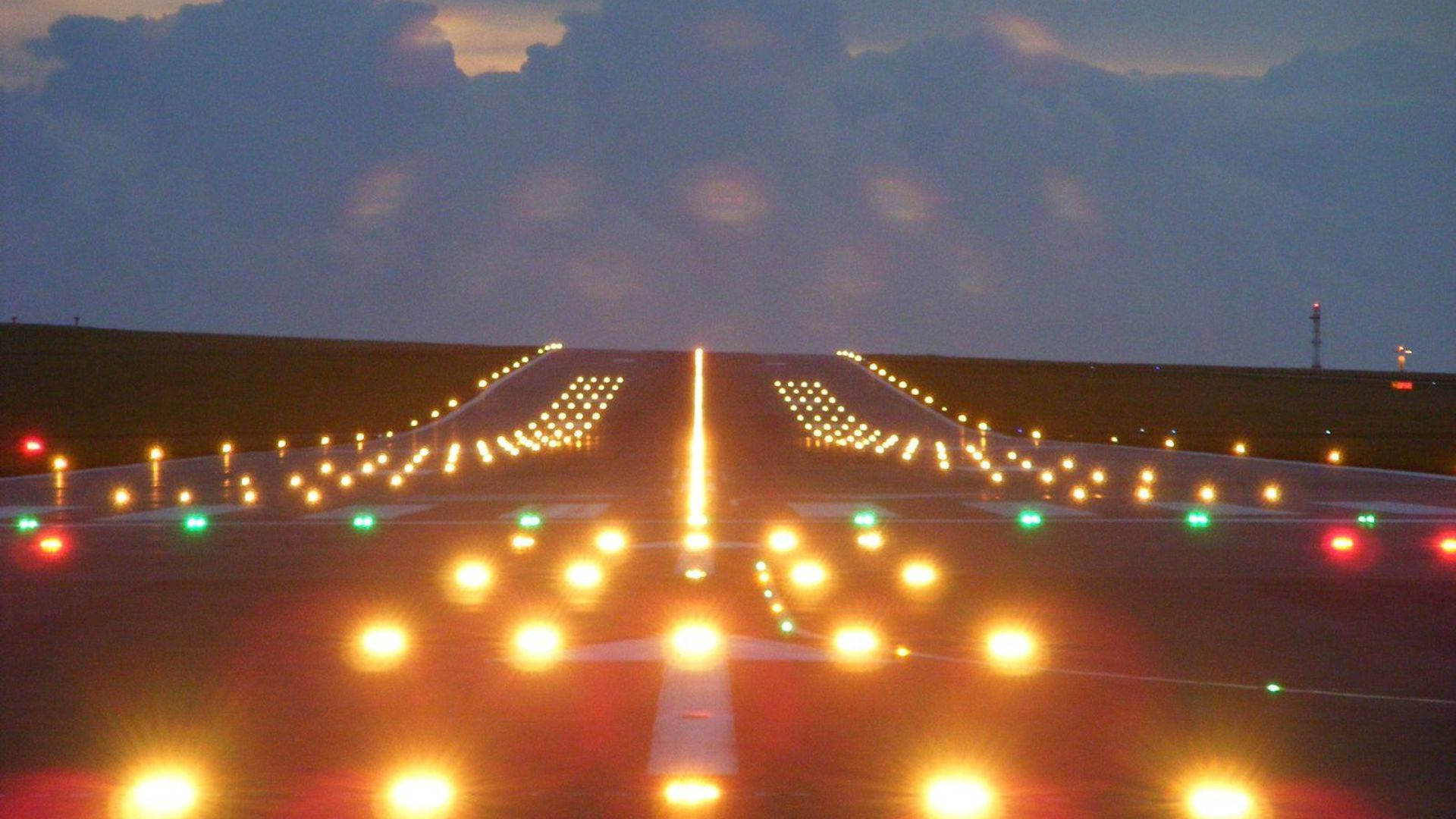 跑道上的橙色燈光 壁紙 — 飛機跑道燈在陰雲密布的黃昏地平線下延伸至暮色天空。