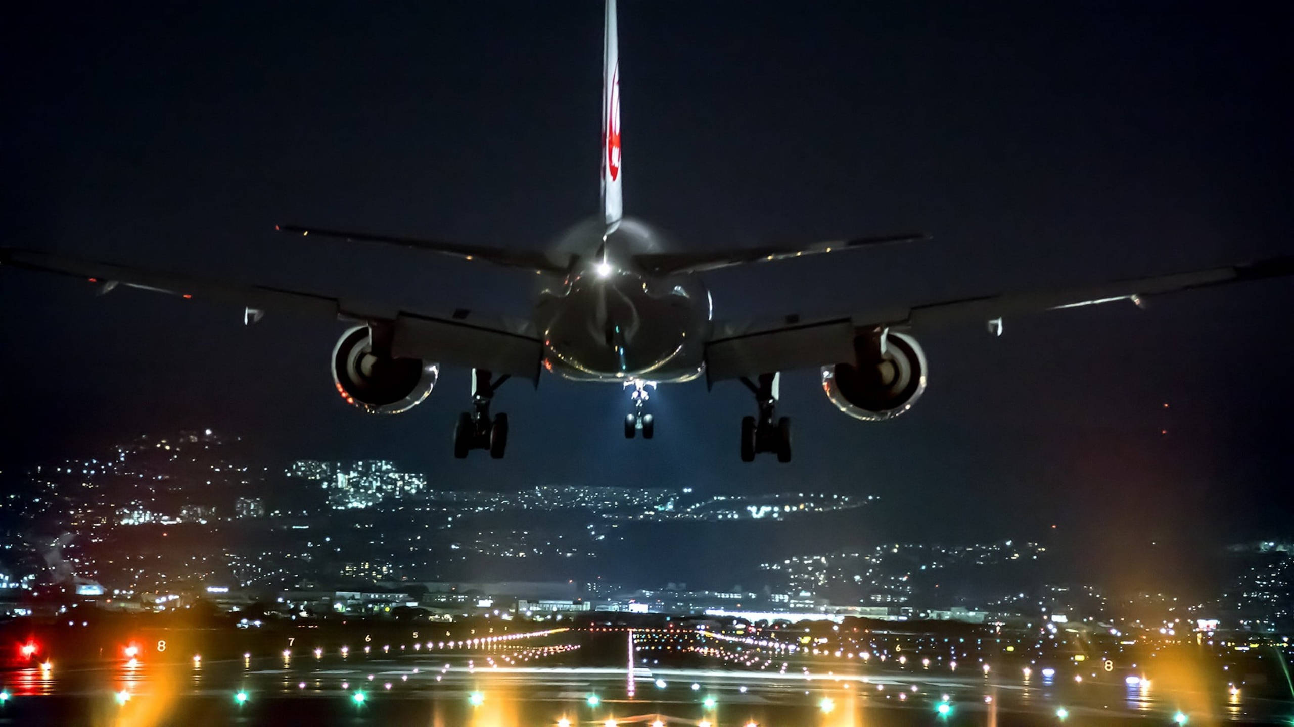 跑道夜景燈光 壁紙 — 一架商用飛機在夜間下降，降落燈亮著，下方是發光的城市景觀。