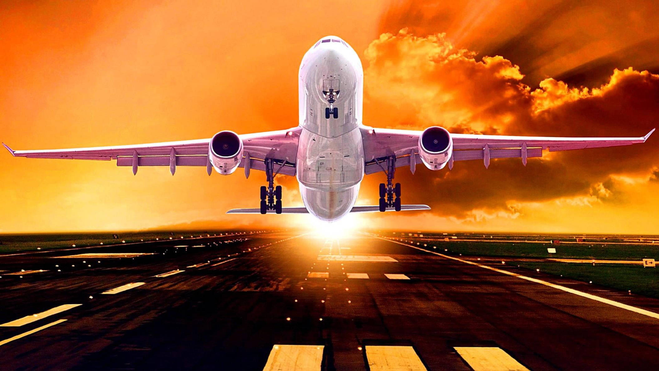 跑道飛機起飛藝術圖 壁紙 — 一架大型客機向著被熾熱橙色夕陽光芒籠罩的跑道下降，上方有戲劇性的雲層。