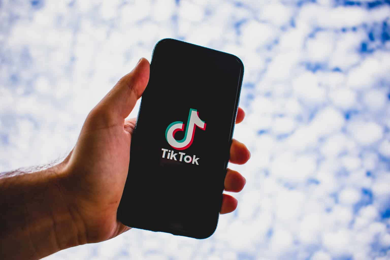 跟隨TikTok最新趨勢 壁紙 — 一隻手拿著智能手機，顯示TikTok標誌，背景是明亮的陰天天空。