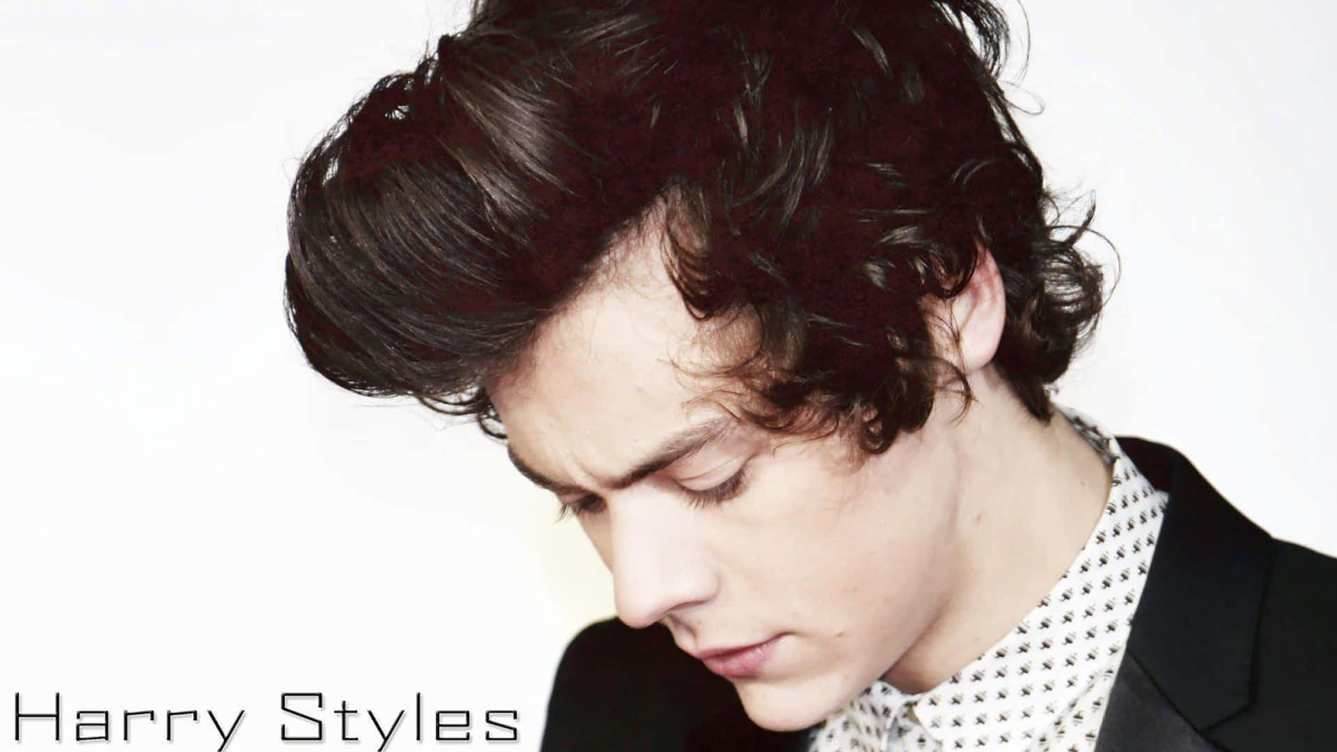 Harry Styles 身穿黑色西裝外套和圖案襯衫，捲髮向下看。