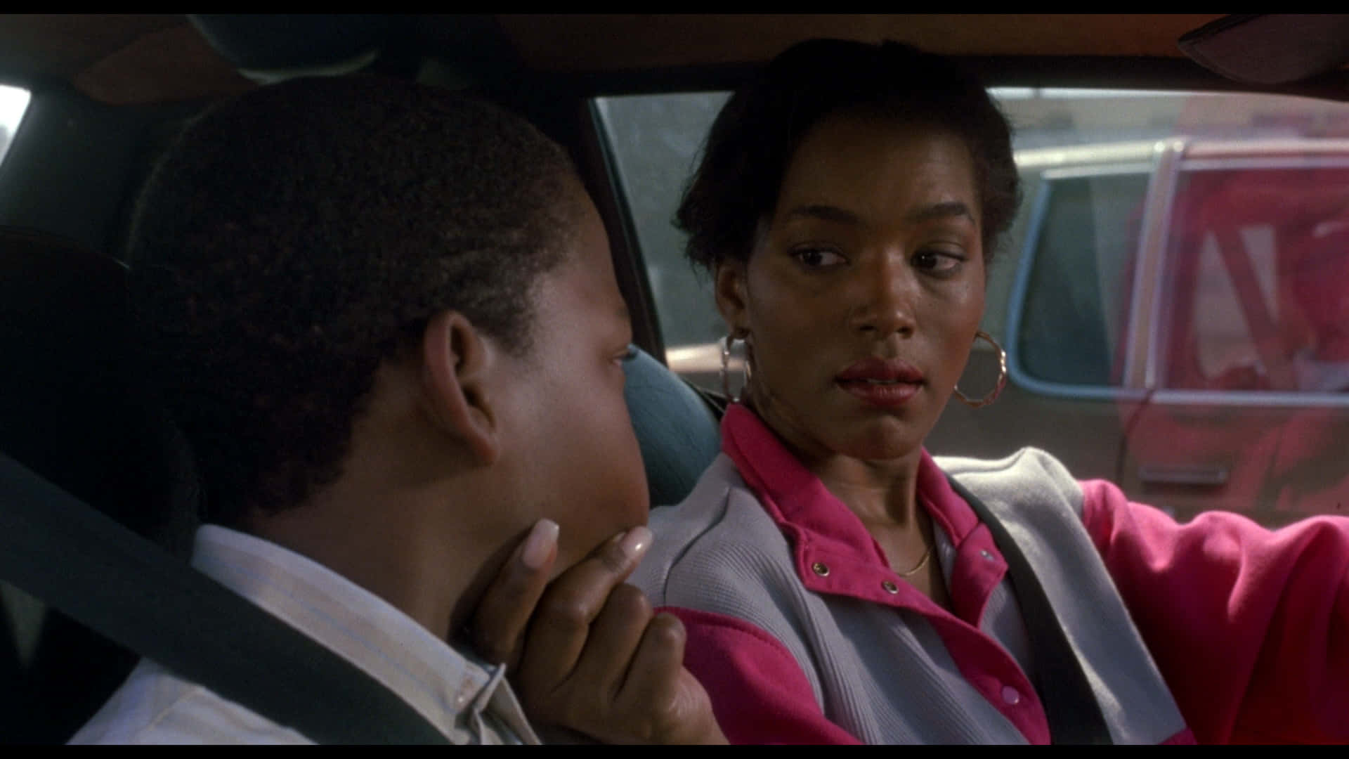跟隨洛杉磯的街道，與《Boyz N The Hood》中的年輕人們同行 壁紙 — 一位身穿粉紅色外套的女性在車內輕柔地觸摸一個小男孩的臉頰，這是一個安靜的時刻。