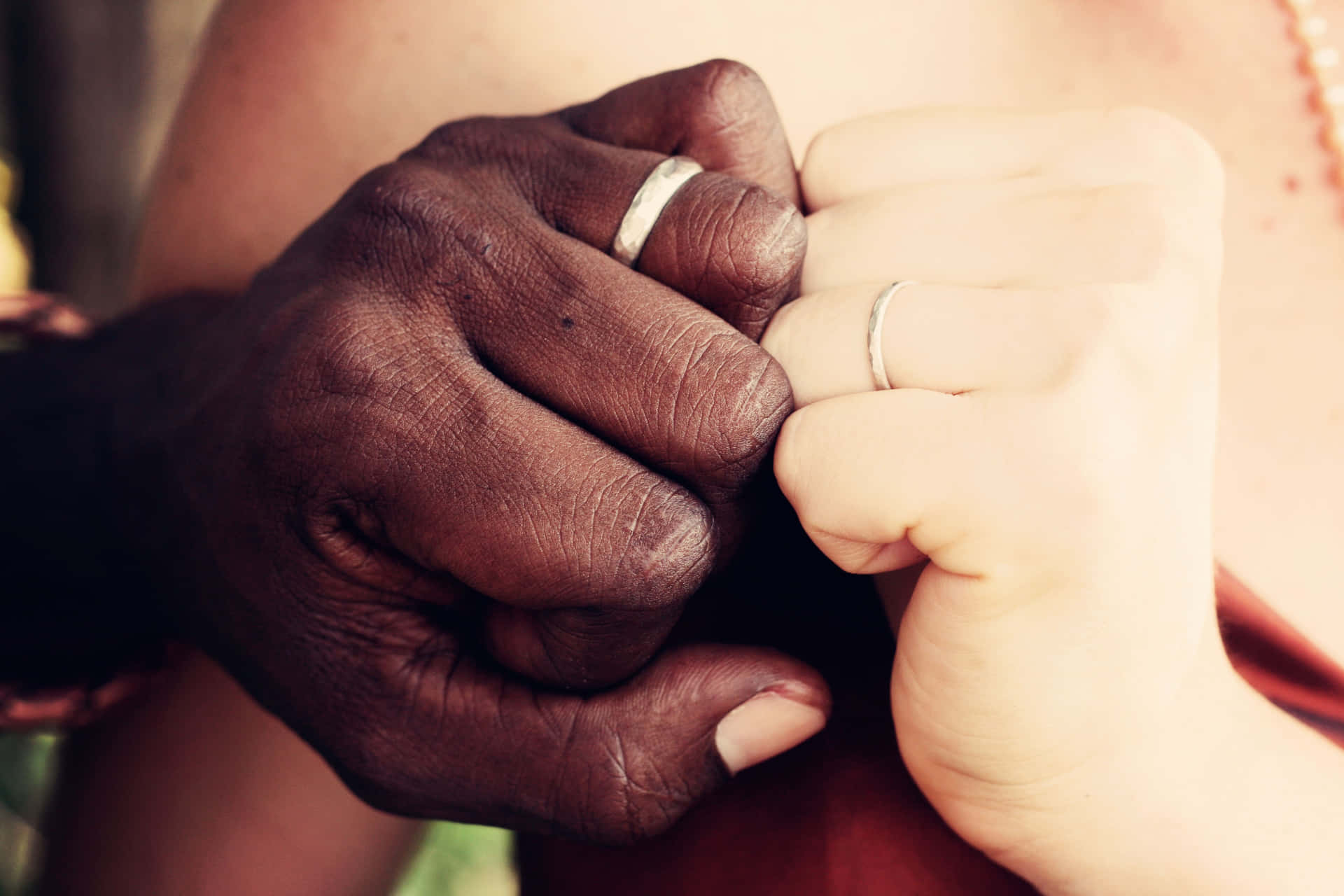 兩隻緊握的手，一深一淺，戴著結婚戒指，展現愛與連結。