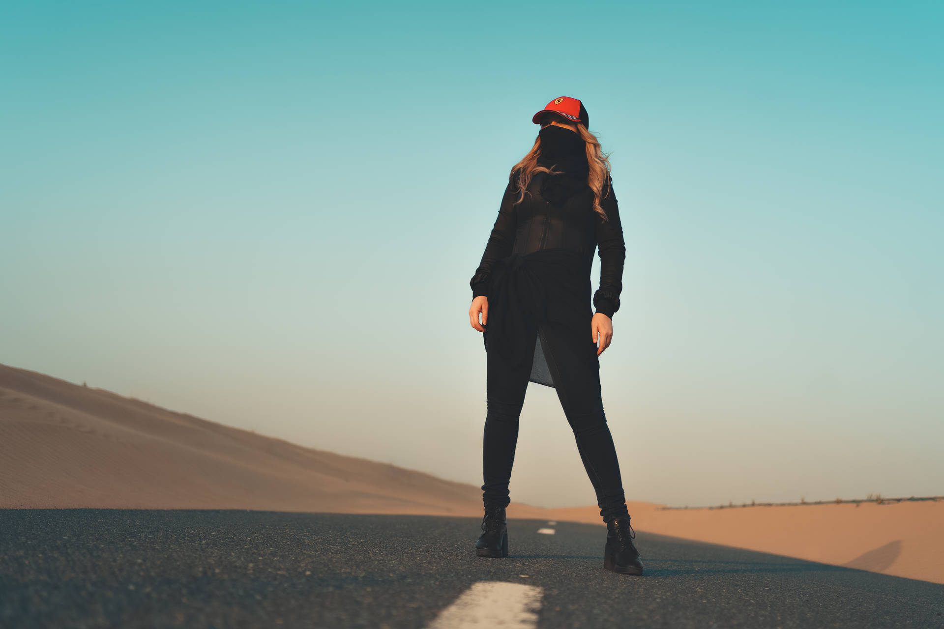 身穿黑色衣服和紅色帽子的人站在日落時分的沙漠公路上。