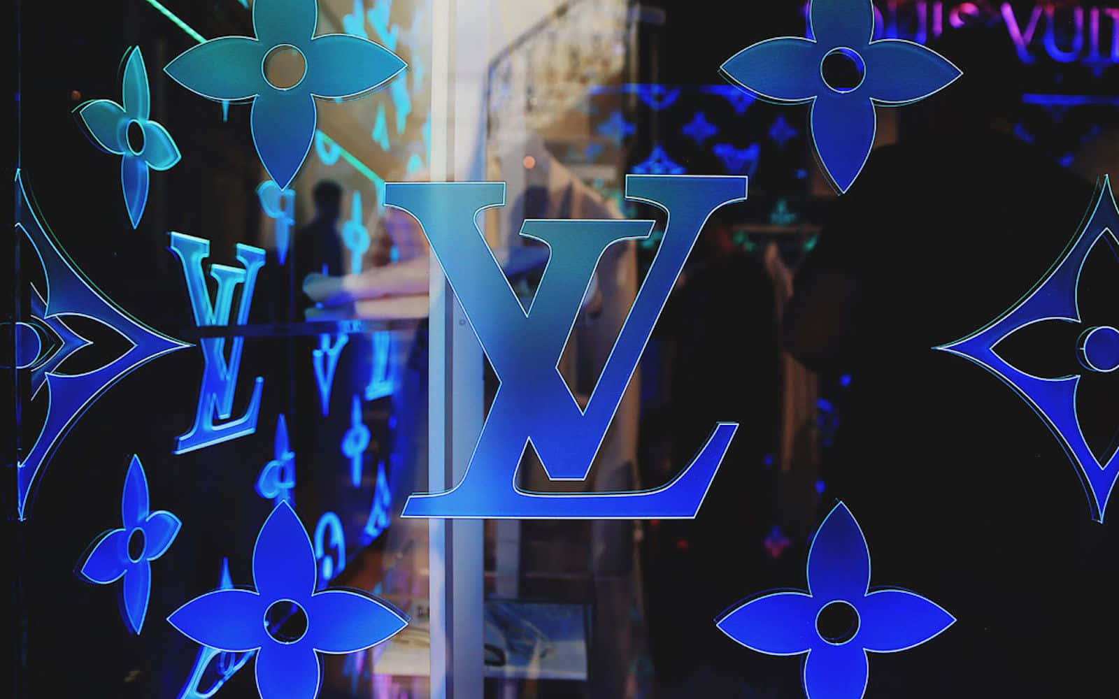 夜間玻璃櫥窗上的藍色 Louis Vuitton 標誌和字母組合圖案。