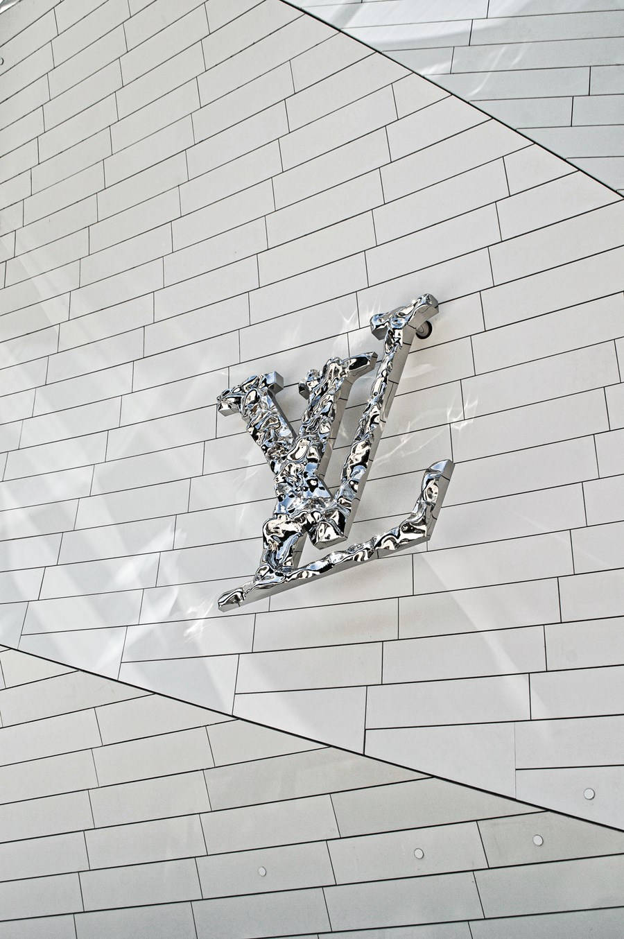 鉻色Louis Vuitton標誌在帶有幾何陰影的白色瓷磚牆上。