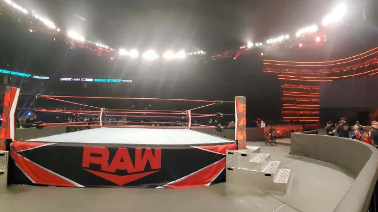 踏入擂台，考驗你的摔角技巧！ 壁紙 — 一個燈光璀璨的WWE RAW摔角擂台，位於座無虛席的場館中央，在戲劇性的舞台燈光下。