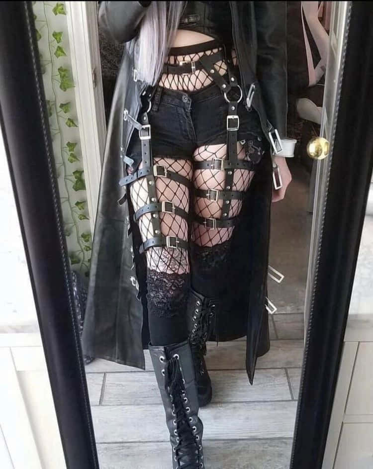 穿著黑色皮革外套和帶金屬扣的漁網襪的人站在鏡子前。