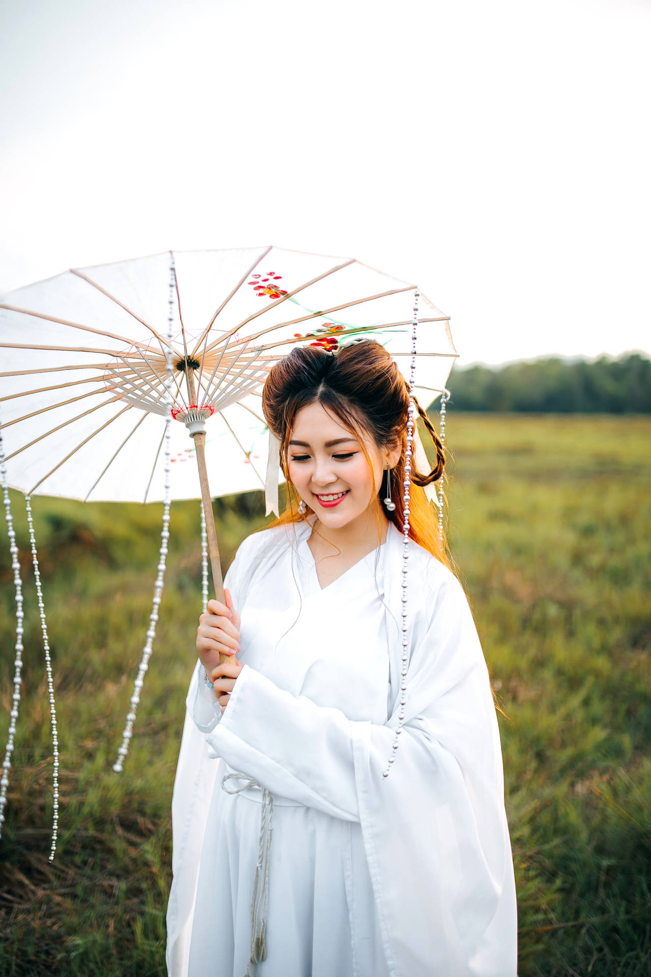 身穿白色傳統長袍的女子在草地上拿著裝飾性陽傘