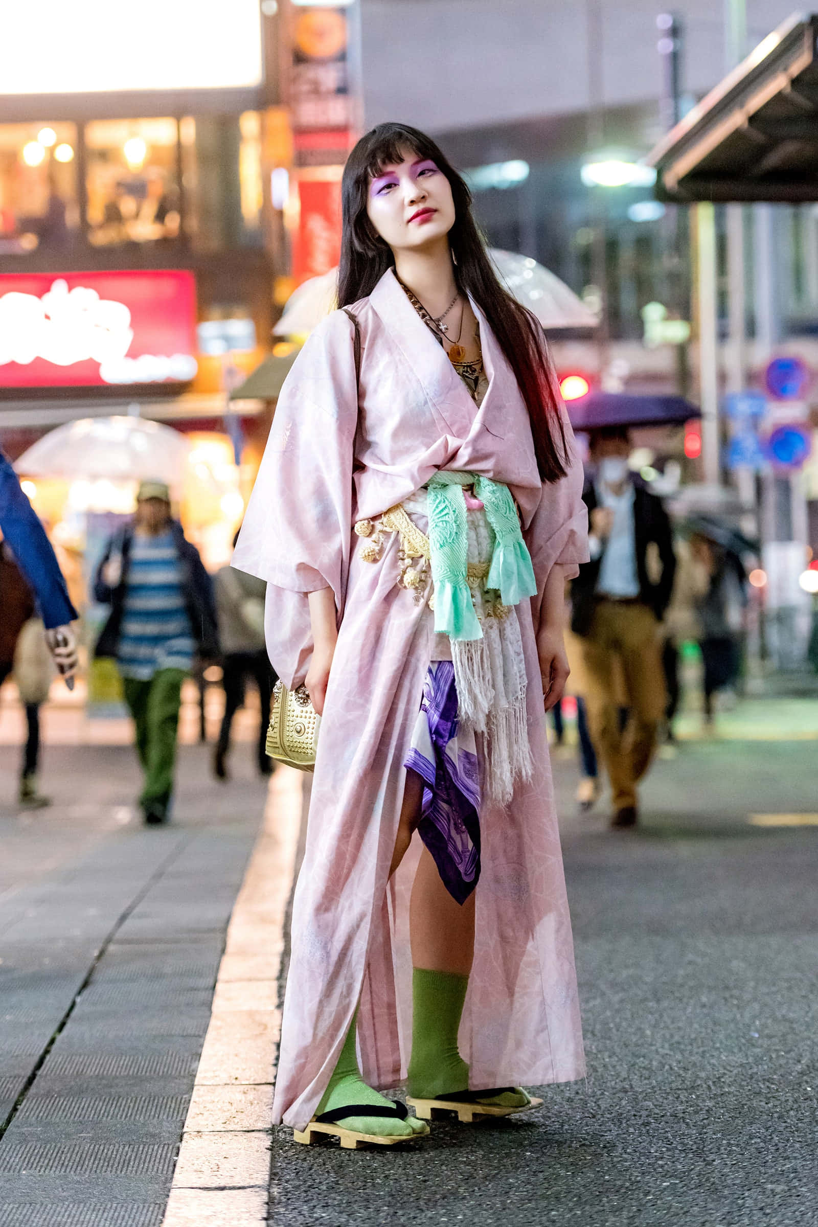 身穿傳統日本和服的男子 壁紙 — 一位身穿粉紅色和服搭配綠色點綴的女性，自信地站在雨夜的東京街頭，周圍是閃爍的霓虹燈招牌和行人。