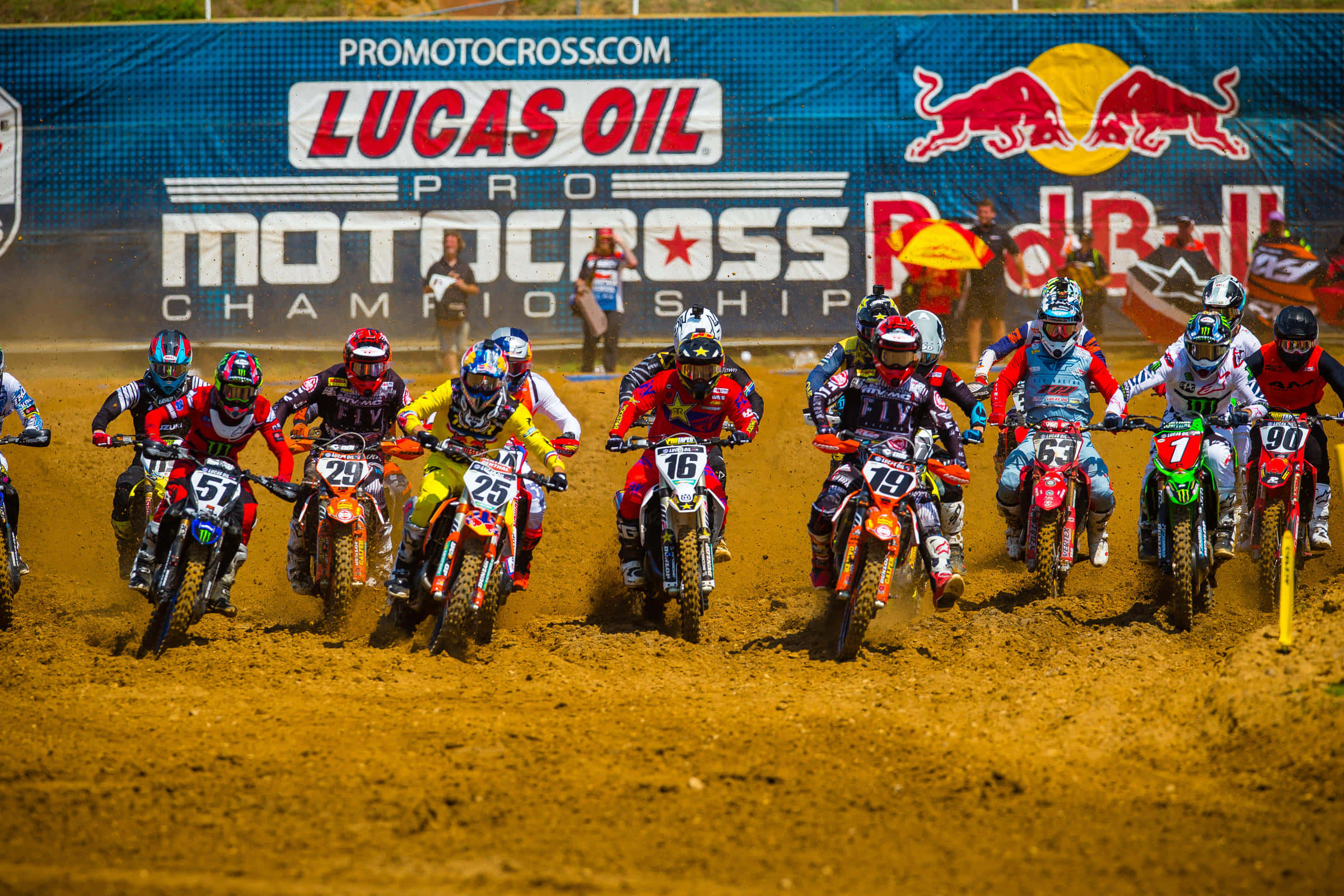 Motocross 桌布 壁紙 — 身穿全套裝備的越野摩托車車手在塵土飛揚的賽道上並肩競速，身後有Lucas Oil和Red Bull的橫幅。