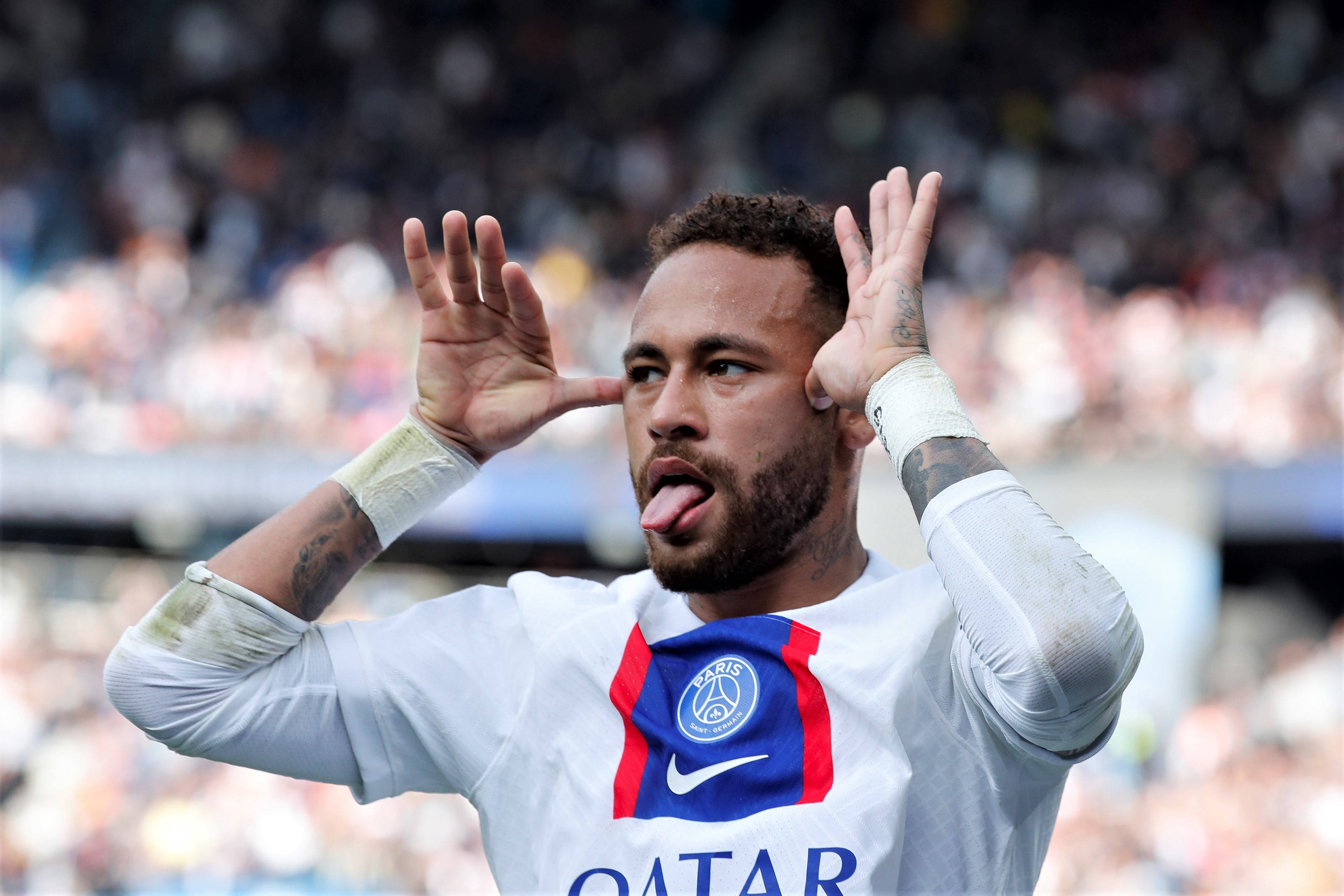 足球 桌布 壁紙 — 身穿巴黎聖日耳曼球衣的足球員尼馬（Neymar Jr）在體育場人群中頑皮地伸出舌頭並舉起雙手。