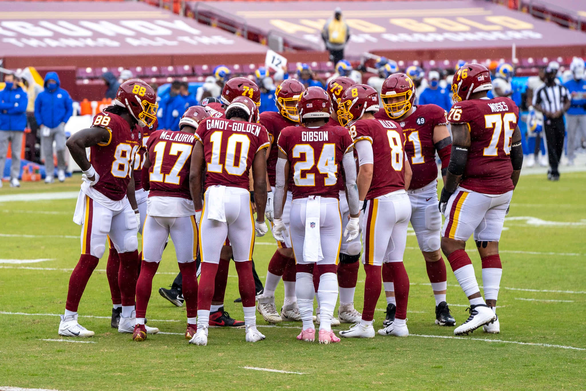 Washington Football 桌布 壁紙 — 身穿栗色和金色球衣的足球運動員在日間比賽中聚集在綠色球場上。