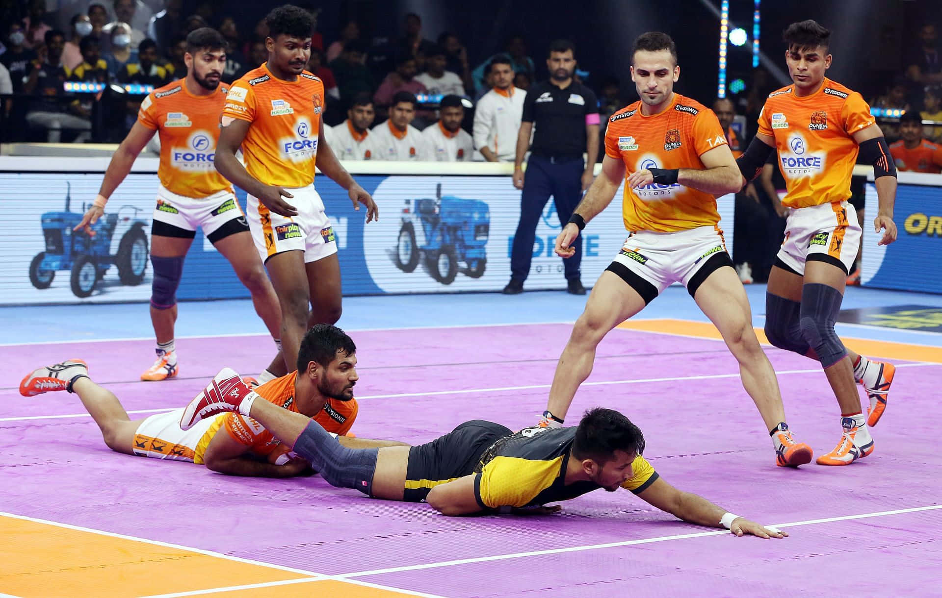 Kabaddi 桌布 壁紙 — 身穿橙色球衣的球員在紫色室內場地上進行激烈的職業卡巴迪比賽。