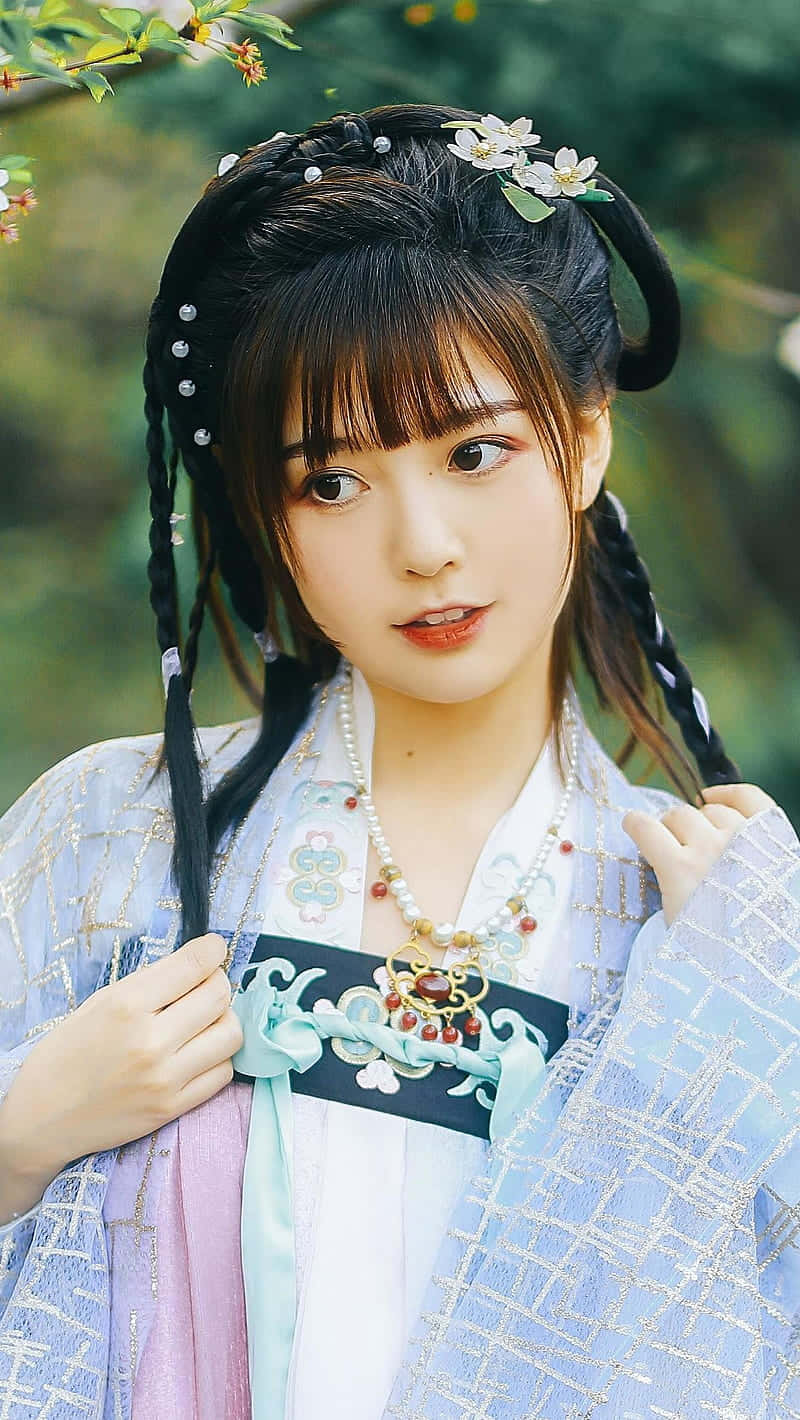 身穿漢服的亞洲女性 壁紙 — 一位身穿傳統漢服、編織辮子點綴花朵的年輕女性，在模糊的綠色花園背景下溫柔微笑。