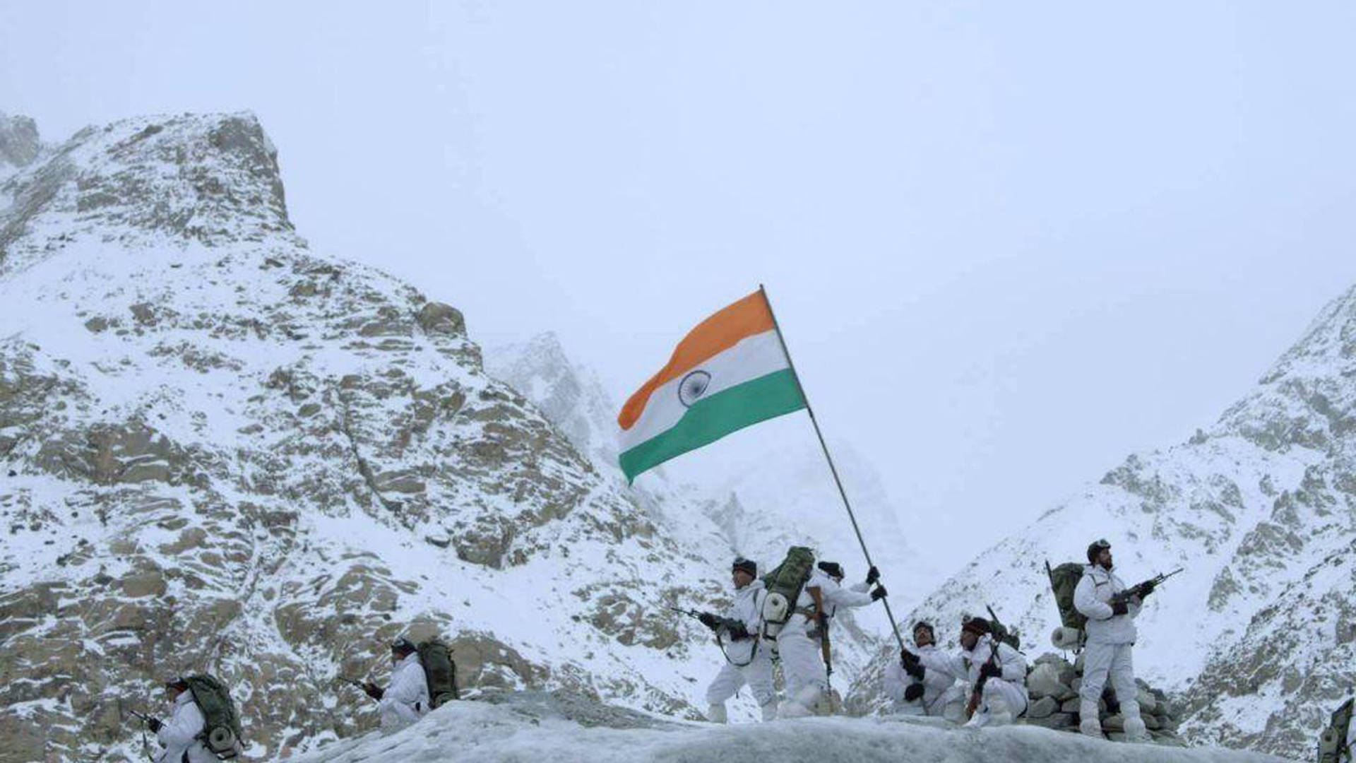 Indian Army 桌布 壁紙 — 身穿白色冬季裝備的印度士兵在灰濛濛的天空下，於白雪覆蓋的山脊上升起國旗。