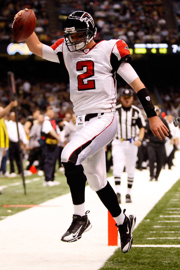 Matt Ryan 桌布 壁紙 — 身穿白色和紅色制服的美式足球四分衛在夜間比賽中，在體育場燈光下躍起傳球。
