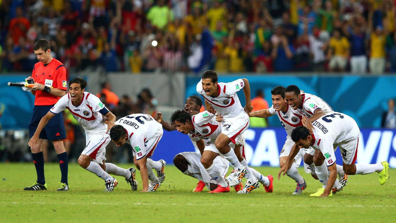 Victory 桌布 壁紙 — 身穿白色球衣的足球運動員在綠色球場上瘋狂慶祝，裁判在附近觀看。
