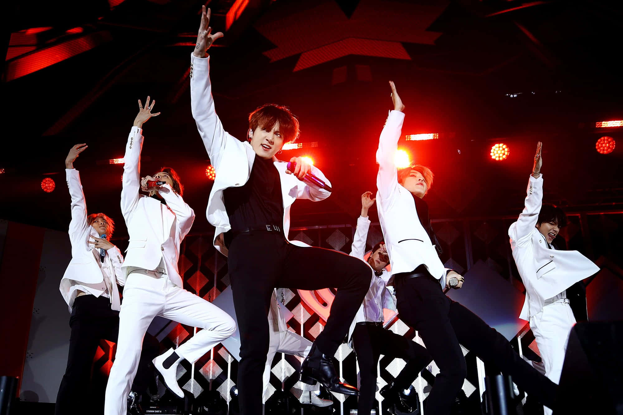 Bts Performance 桌布 壁紙 — 身穿白色西裝的K-pop表演者在紅色舞台燈光下，於一場充滿活力的演唱會中擺出動態姿勢。