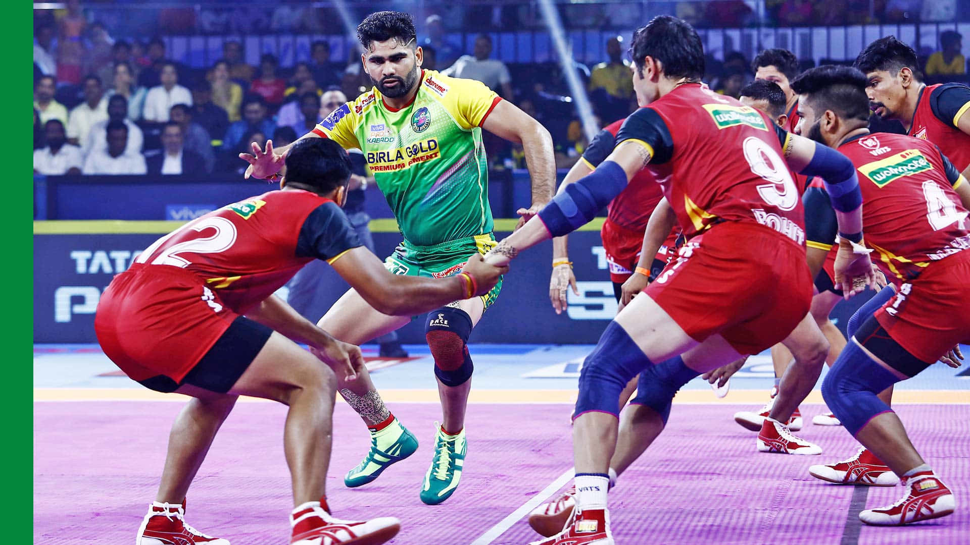 Kabaddi 桌布 壁紙 — 身穿紅色和綠色球衣的排球運動員在充滿活力的紫色場地上，在明亮的體育館燈光下激烈爭奪球權。