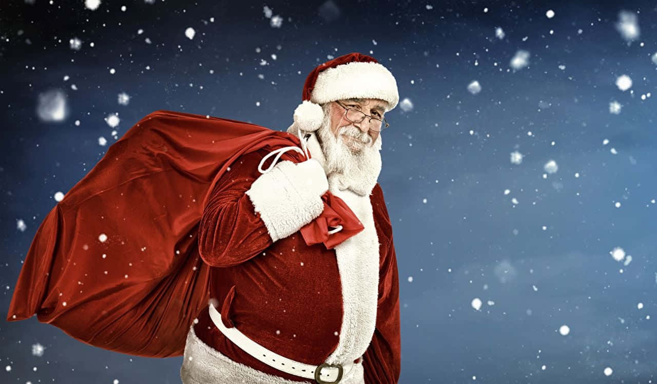 Santa Claus 桌布 壁紙 — 身穿紅色天鵝絨套裝的聖誕老人，在雪花飄落的雪夜天空中扛著一個巨大的袋子。