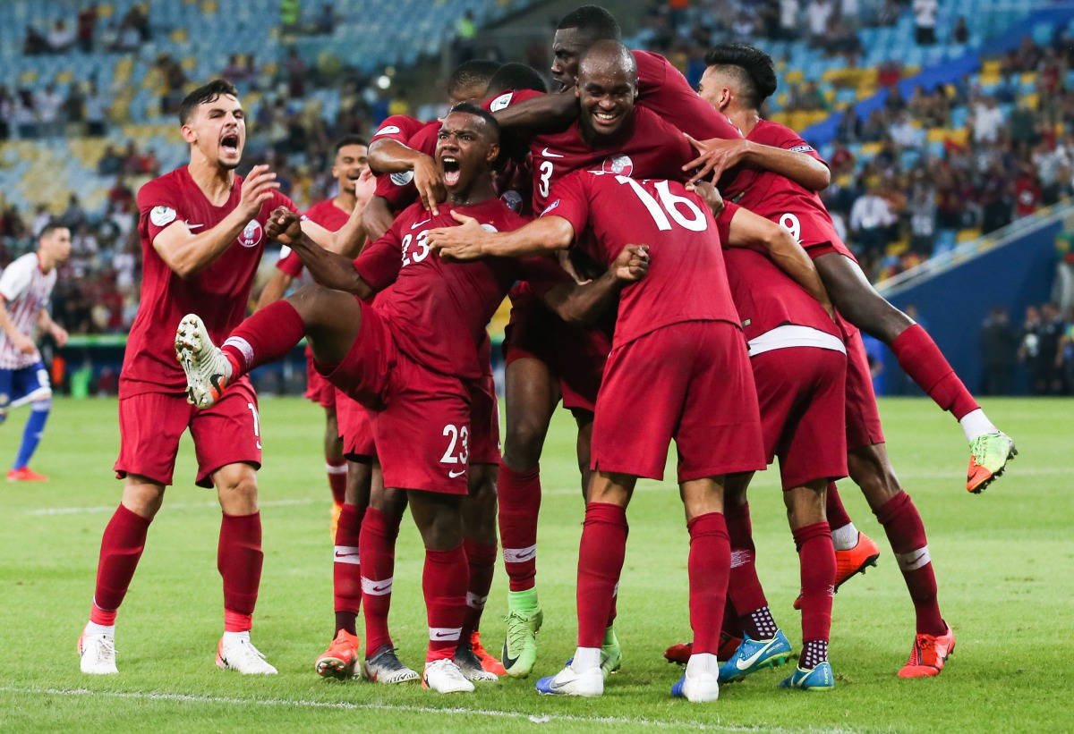 Qatar 桌布 壁紙 — 身穿紅色球衣的足球員在球場燈光下，於充滿活力的綠色草地上瘋狂慶祝入球，互相擁抱。