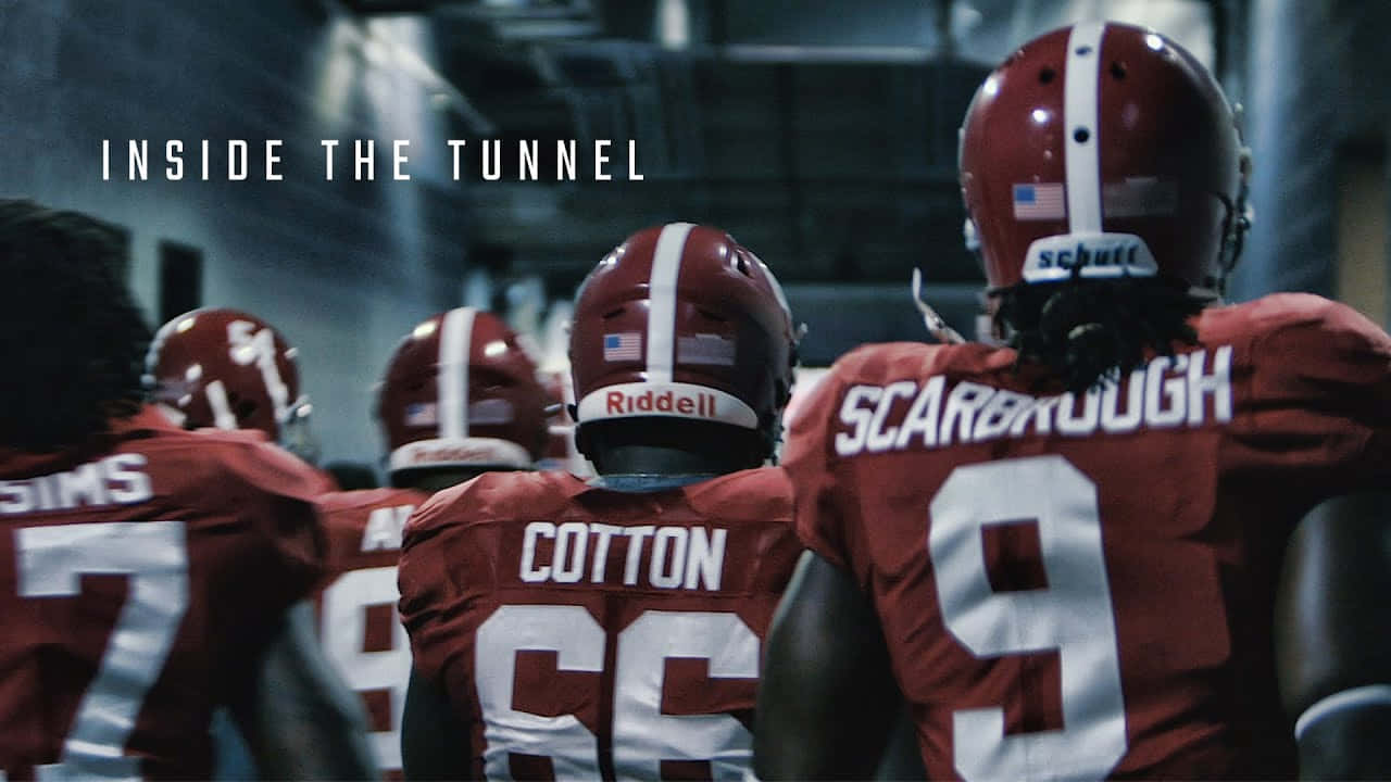 Roll Tide! 壁紙 — 身穿紅色球衣的足球運動員在昏暗的隧道中，帶著專注的決心走向球場。