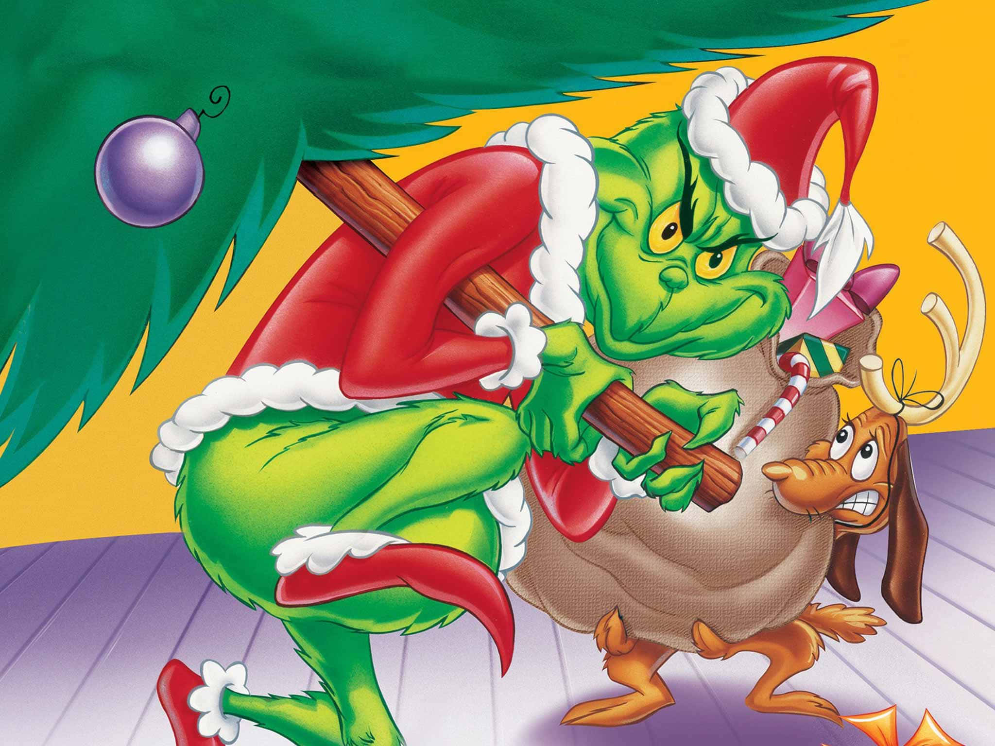The Grinch 桌布 壁紙 — 身穿紅色聖誕老人套裝的鬼靈精扛著一個麻袋，他的狗麥克斯在聖誕樹下看著。