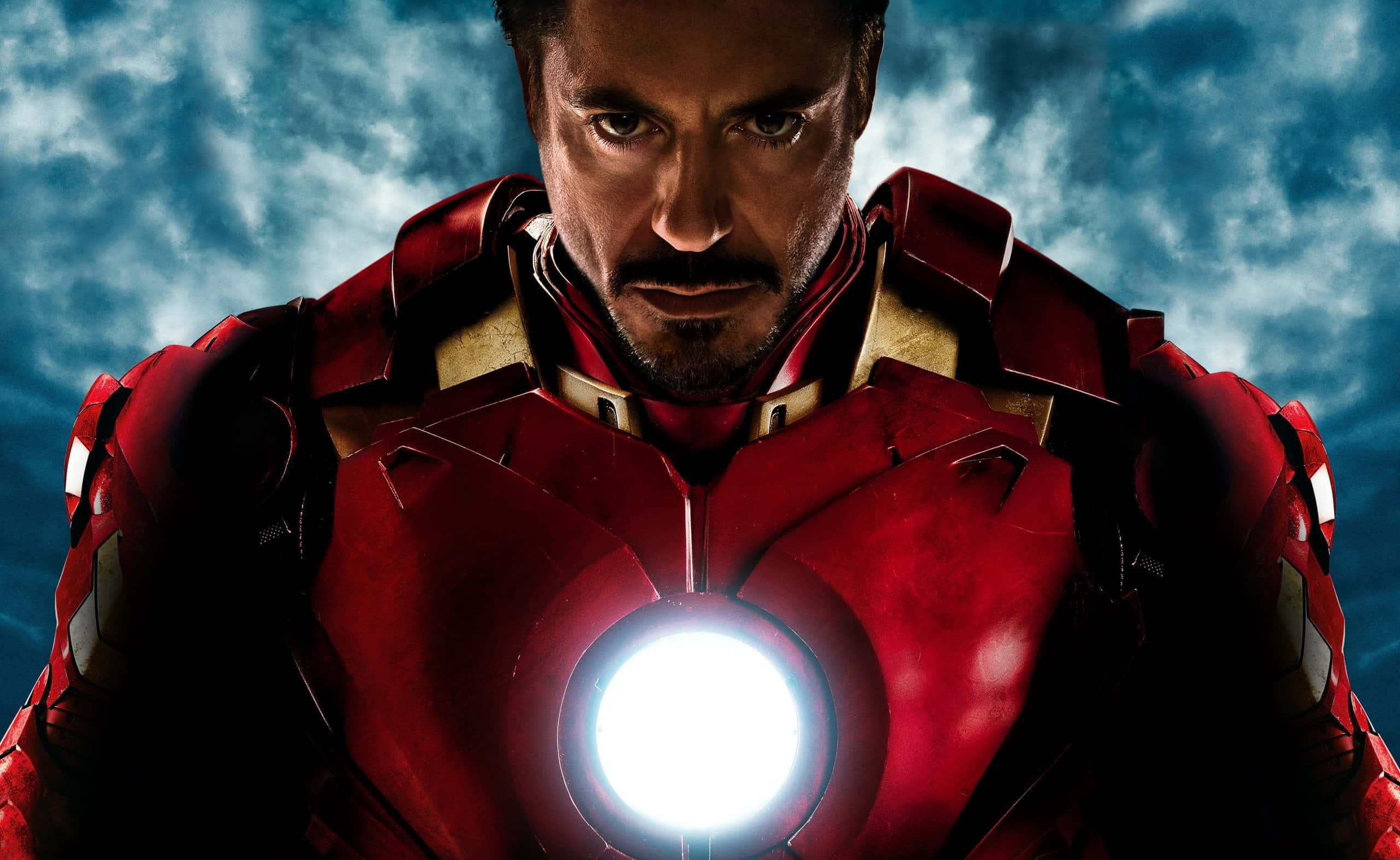 Superhero Movies 桌布 壁紙 — 身穿紅色裝甲的鐵甲奇俠，在風暴藍天下，帶著發光的弧形反應堆，凝視著。