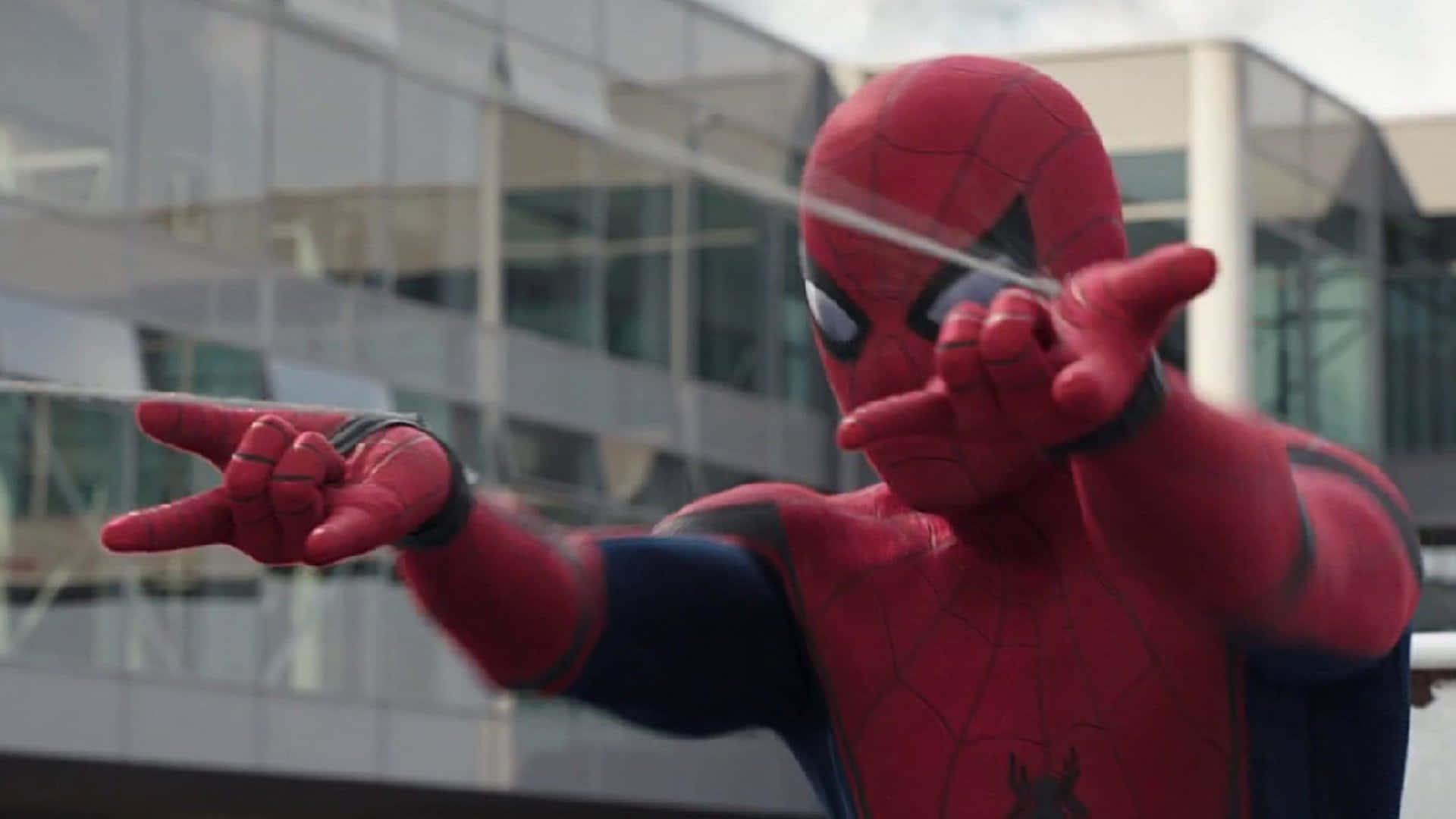 Spider-man Web Shooter 桌布 壁紙 — 身穿紅藍戰衣的蜘蛛俠，在玻璃大廈背景下從手中射出蜘蛛絲。