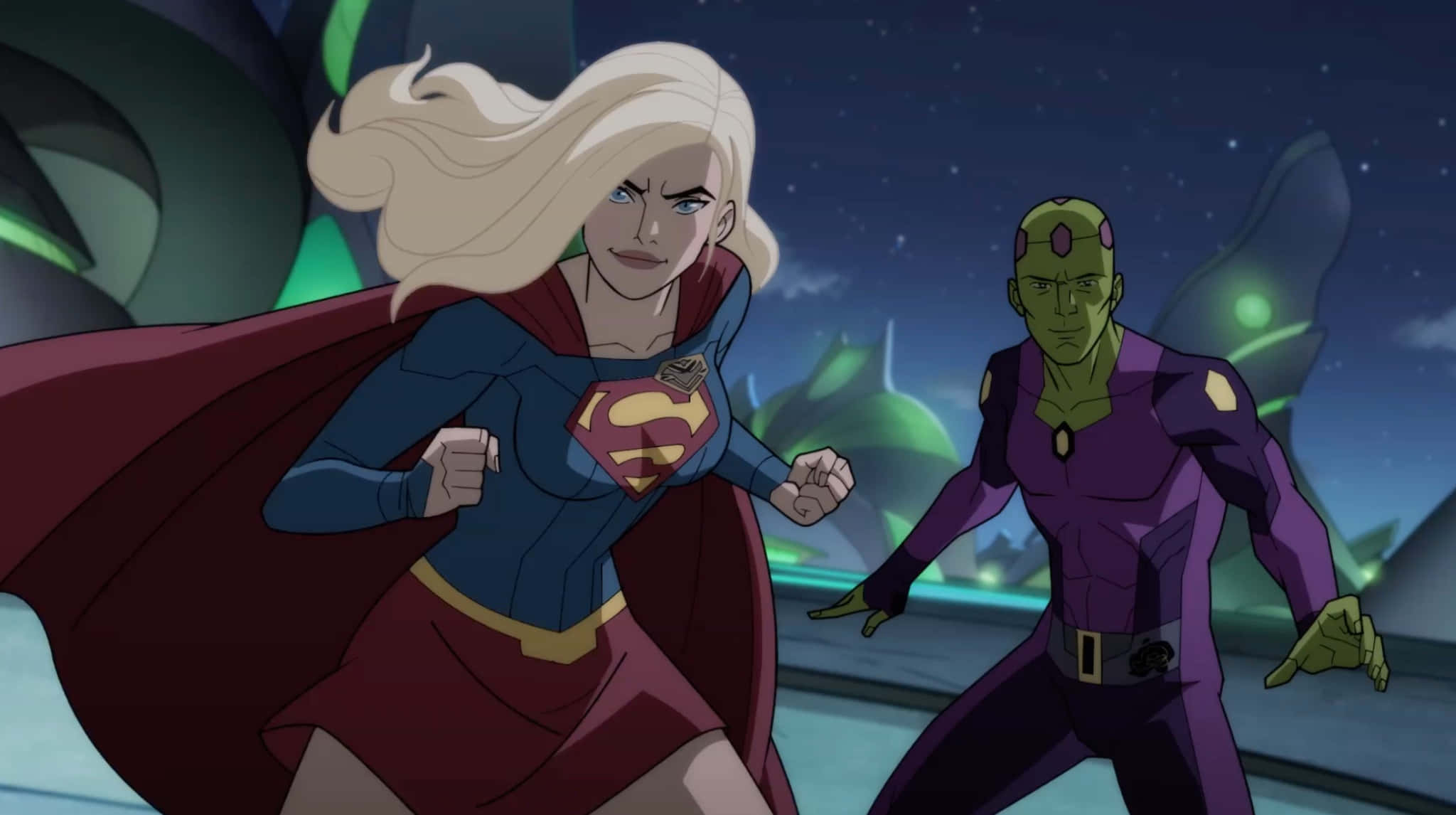 Superman Unbound 桌布 壁紙 — 身穿藍紅戰衣的超級女孩披風飄揚向前奔跑，紫色戰衣的綠色皮膚反派在星空夜空下追趕她。