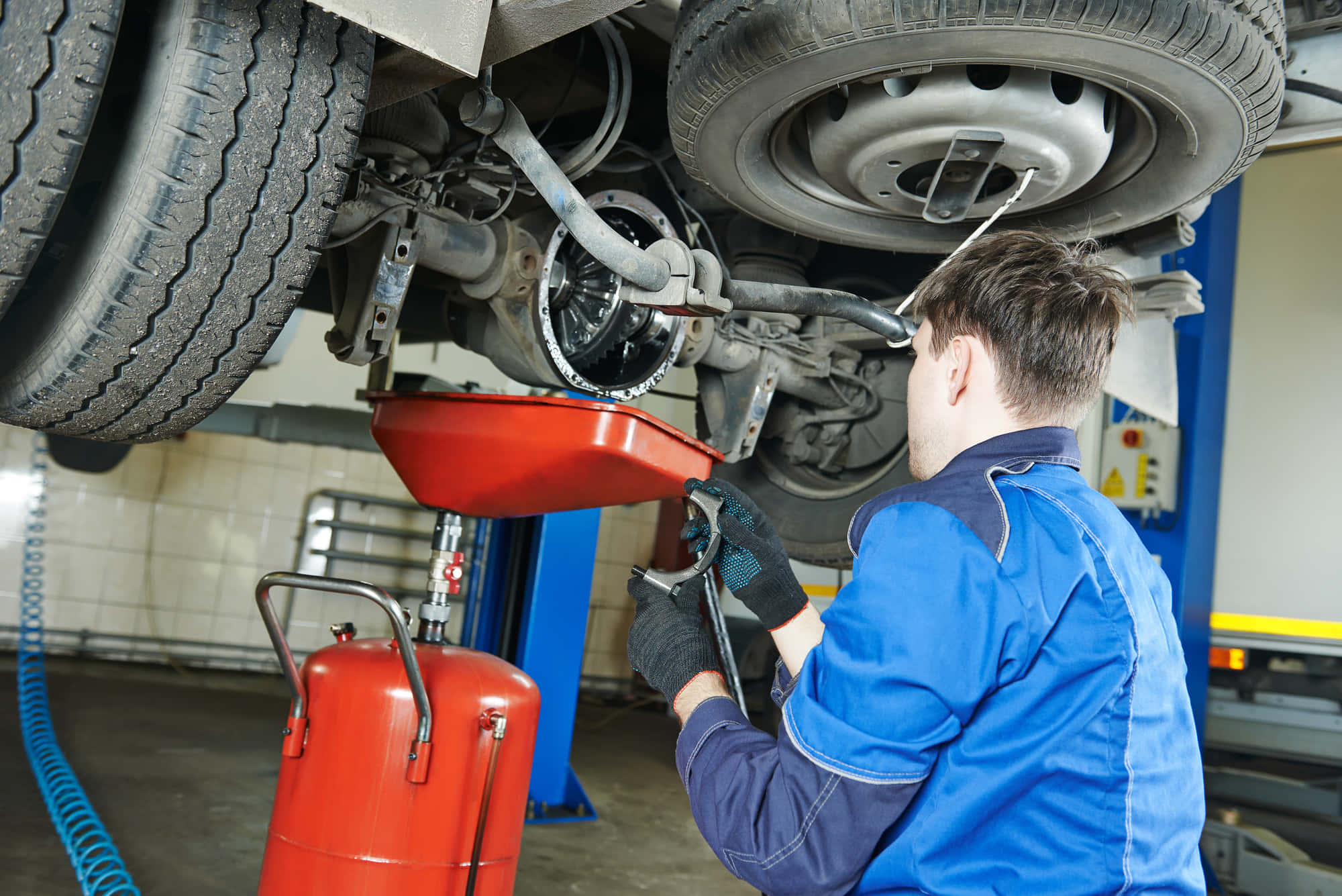 Car Repair 桌布 壁紙 — 身穿藍色制服的機械師在車庫燈光下從升降的汽車中排放引擎機油。