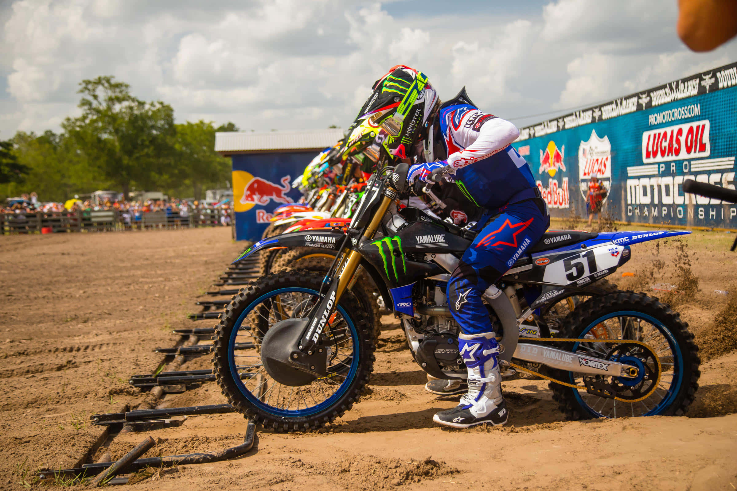 Motocross 桌布 壁紙 — 身穿藍色裝備的越野電單車手在泥地賽道上傾斜入彎，背景有觀眾和贊助商橫幅。
