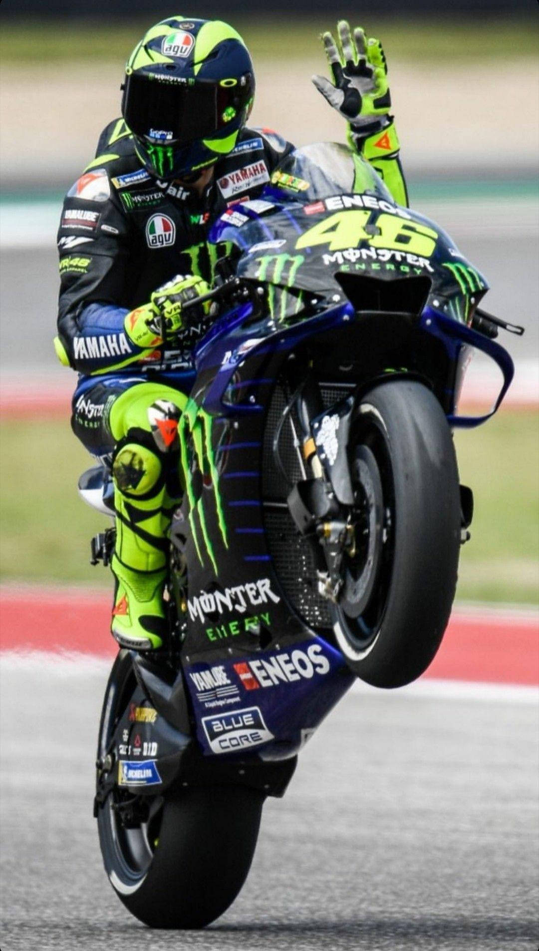 Monster Energy 桌布 壁紙 — 身穿螢光綠色裝備的電單車手在賽道上用藍色Yamaha賽車表演前輪離地。