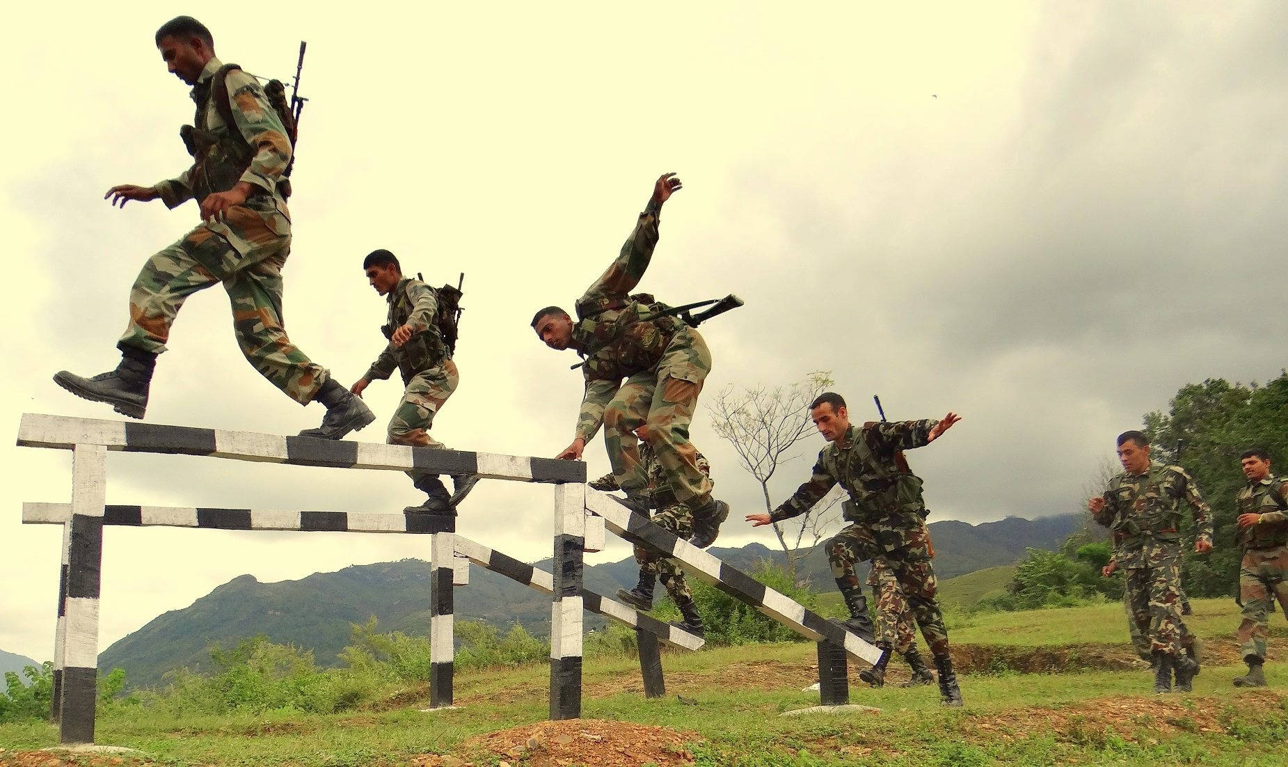 Indian Army 桌布 壁紙 — 身穿迷彩服的士兵在崎嶇的戶外訓練中跳過黑白條紋障礙物。