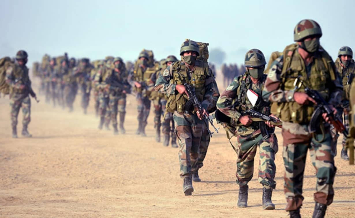 Indian Army 桌布 壁紙 — 身穿迷彩裝備的士兵在煙霧瀰漫的天空下，以隊形穿過塵土飛揚的沙漠景觀。