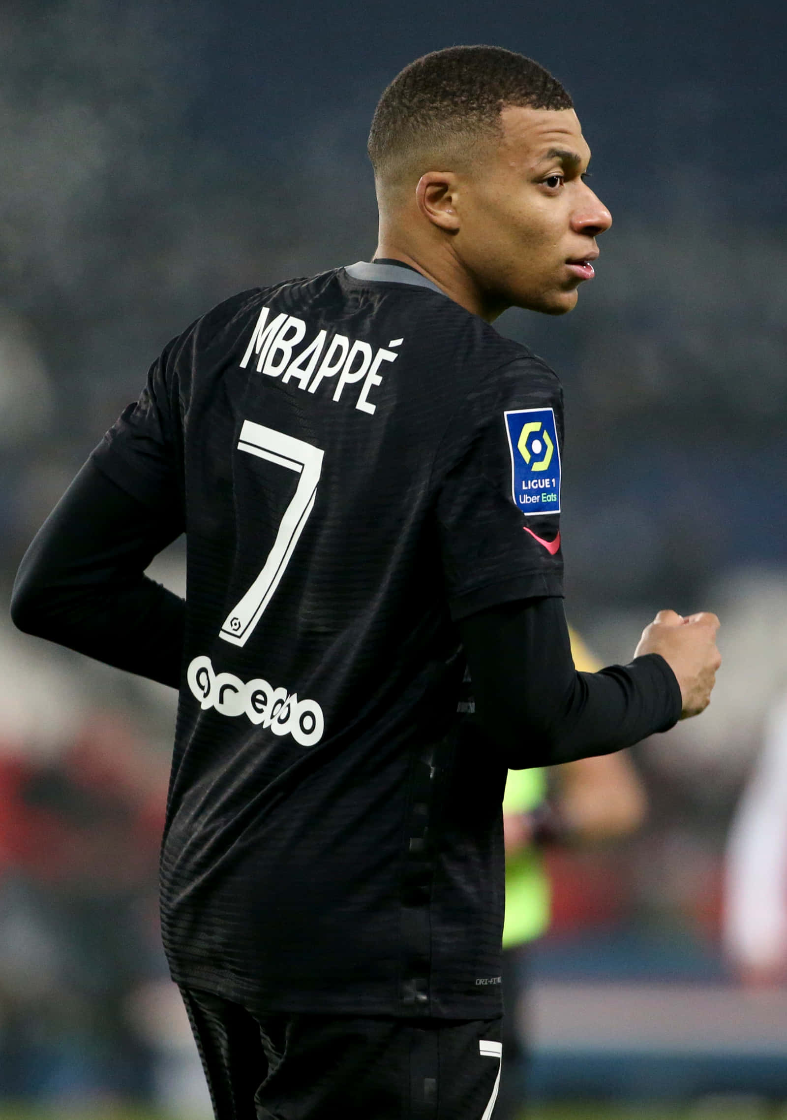 Mbappe 桌布 壁紙 — 身穿黑色7號球衣的足球員基利安·麥巴比在明亮燈光下的球場上轉身邁步。