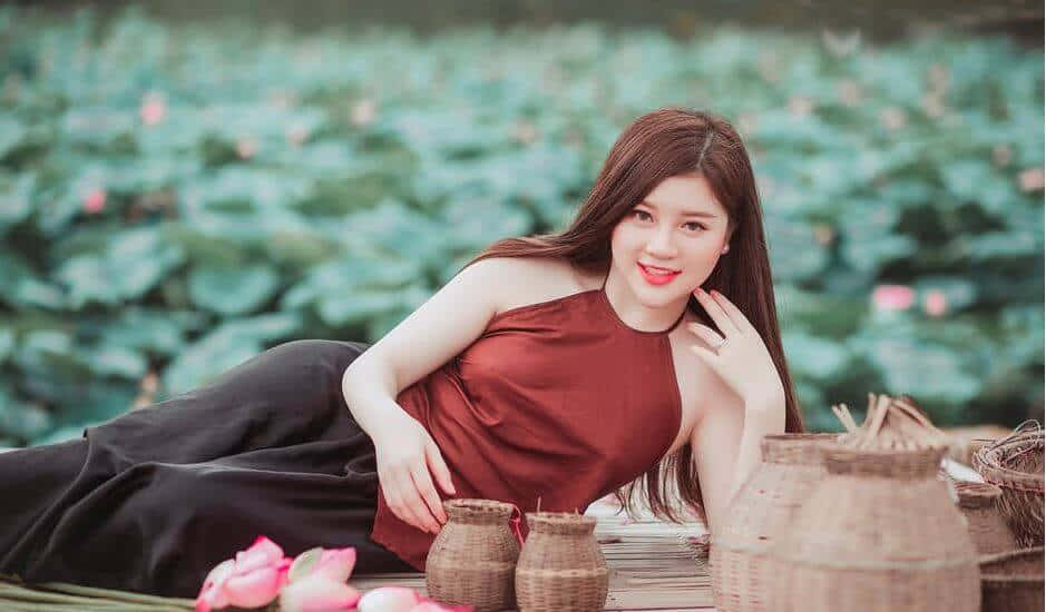躺臥美女側影美照 壁紙 — 一位身穿紅色上衣的女性，在寧靜的蓮花池中的竹筏上，優雅地躺在編織籃子旁邊。