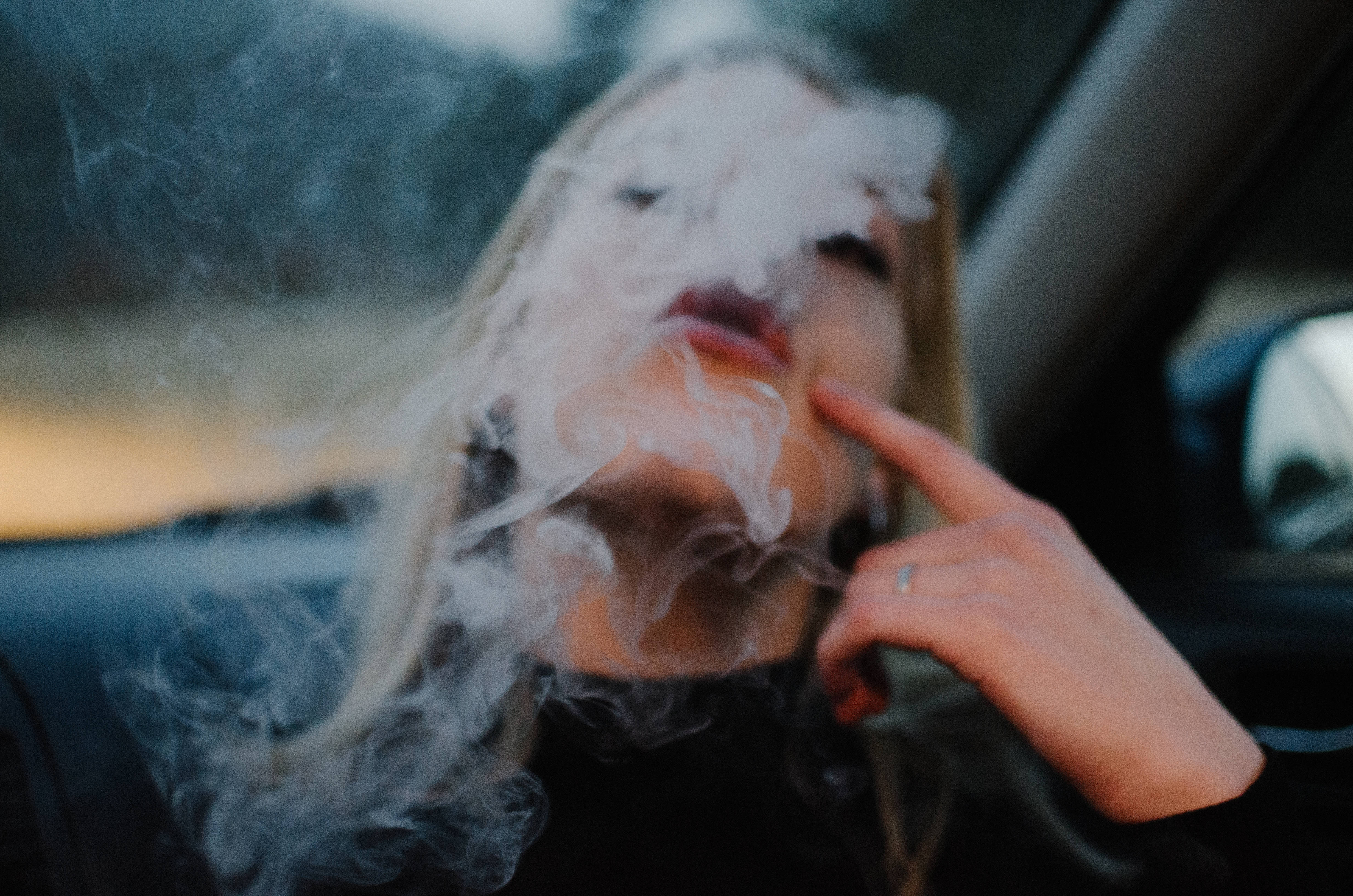 車內吸大麻 壁紙 — 一名金髮人士在車內呼出濃煙，同時指著自己的嘴唇。