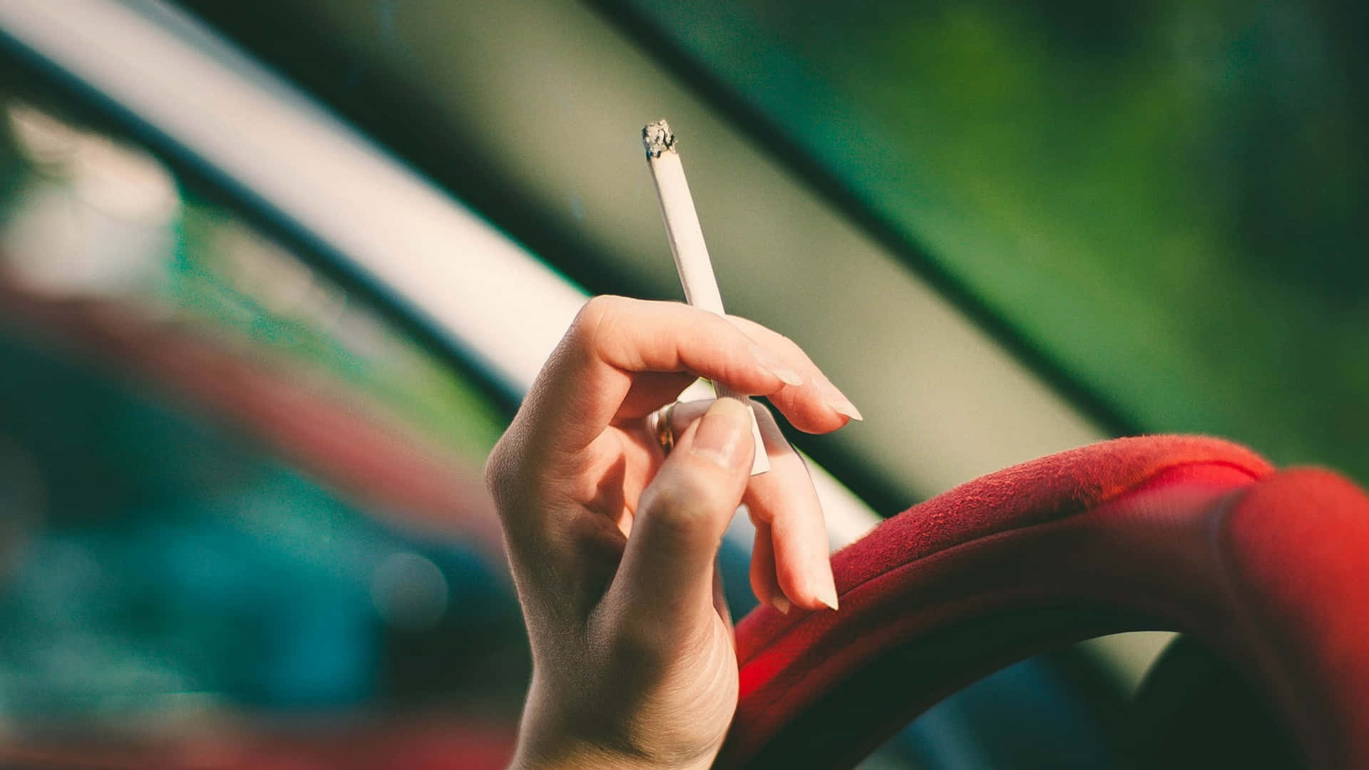 手喺車入面揸住點着咗嘅煙，紅色座椅，綠色背景。