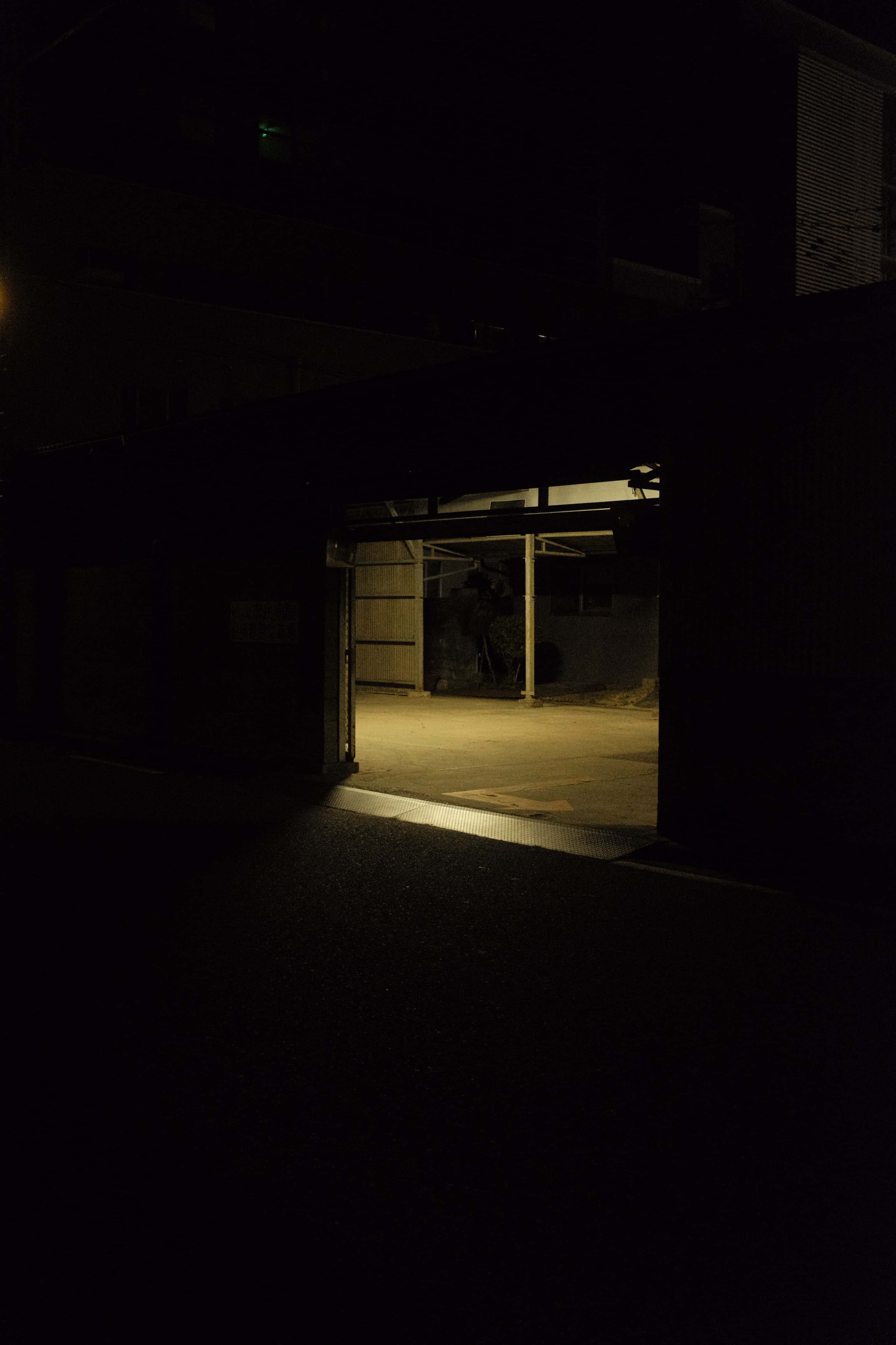 車庫門地庫背景 壁紙 — 夜晚一條狹窄的小巷被一盞溫暖的燈光照亮，顯露出混凝土地板和金屬結構。