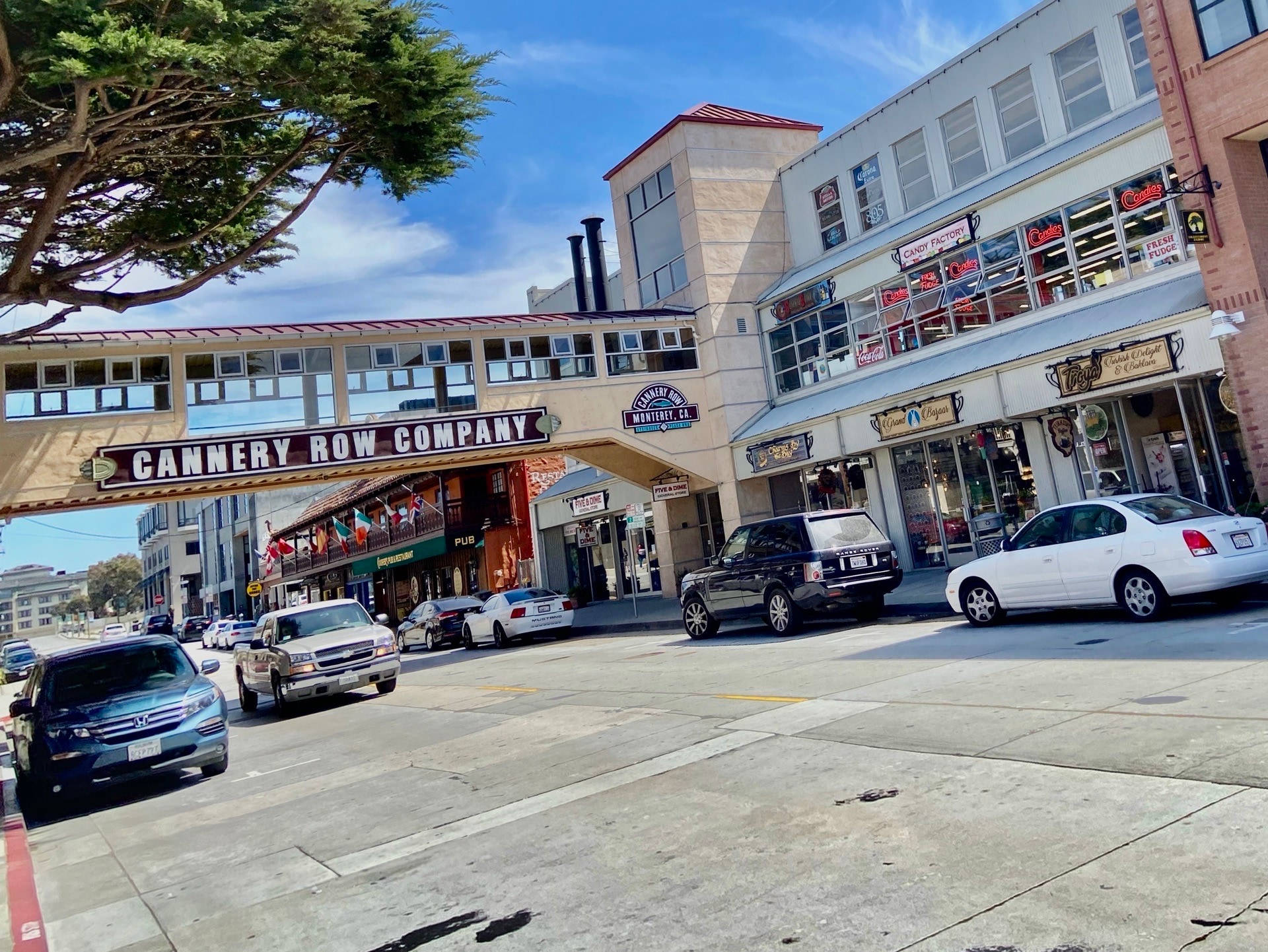 車輛穿行坎農行街 壁紙 — 坎納利街的陽光街道場景，汽車沿著商店停放，藍天白雲。