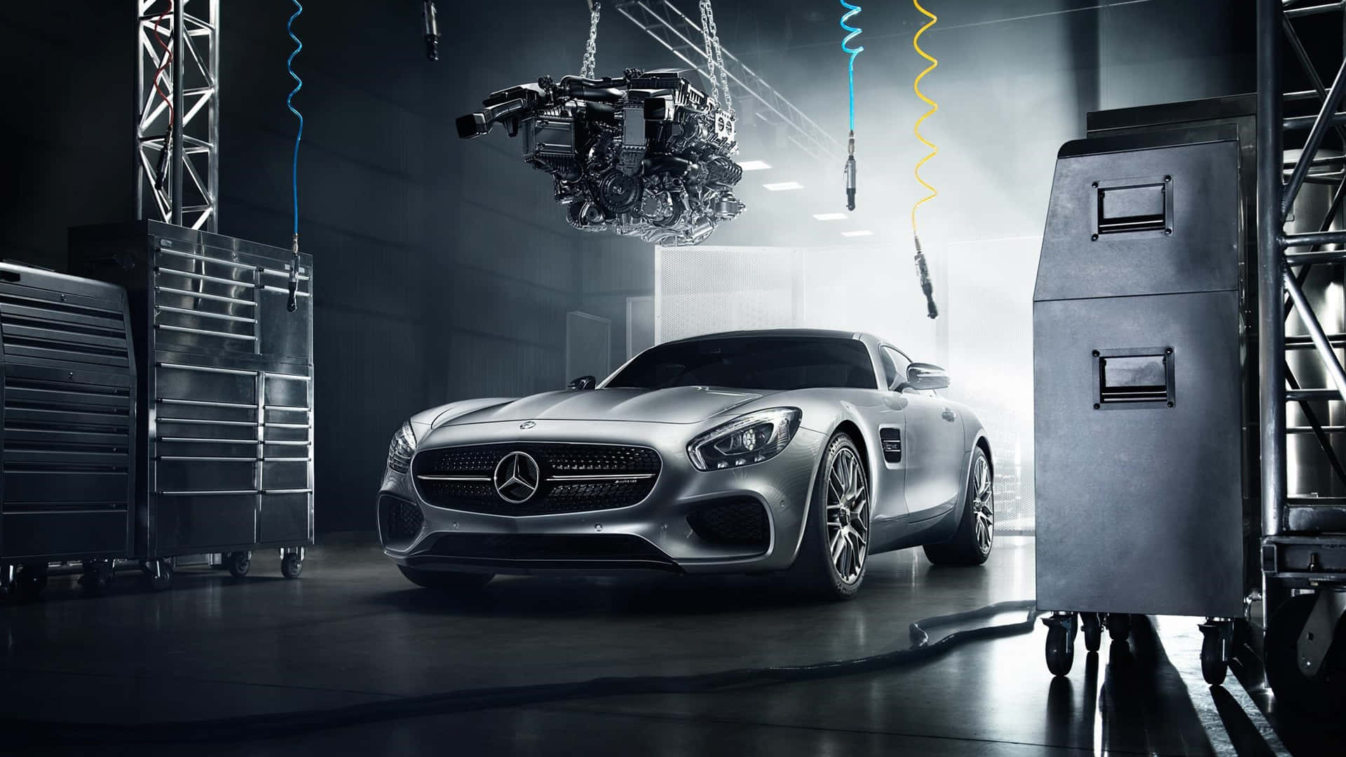 車輪上的華麗優雅 — 梅賽德斯-奔馳 壁紙 — 一輛時尚的銀色 Mercedes-AMG GT 跑車在戲劇性的工作室燈光下閃閃發光，上方懸掛著引擎，位於高科技車庫中。