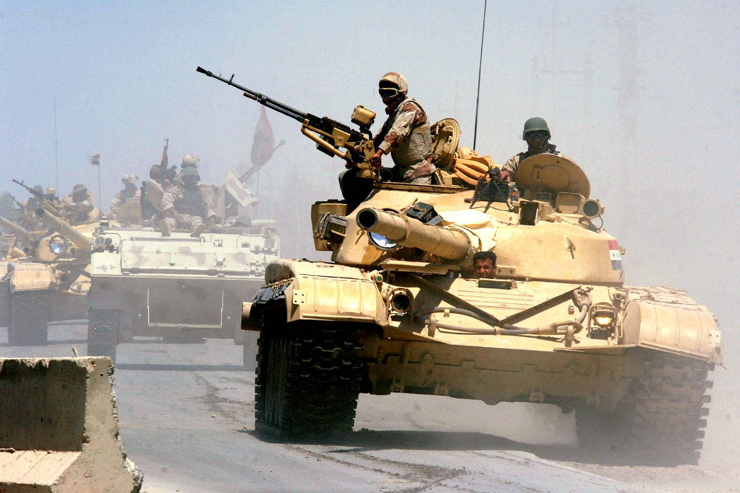 軍用坦克與車輛 壁紙 — 軍用坦克與身穿沙漠迷彩的士兵在朦朧天空下穿越塵土飛揚的地形前進。