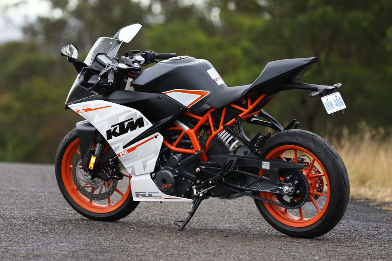 輪上腎上腺素激增 - KTM性能摩托車 壁紙 — 一架型格黑色橙色KTM RC 250電單車停泊在碎石路上，背景有模糊的綠色樹木。