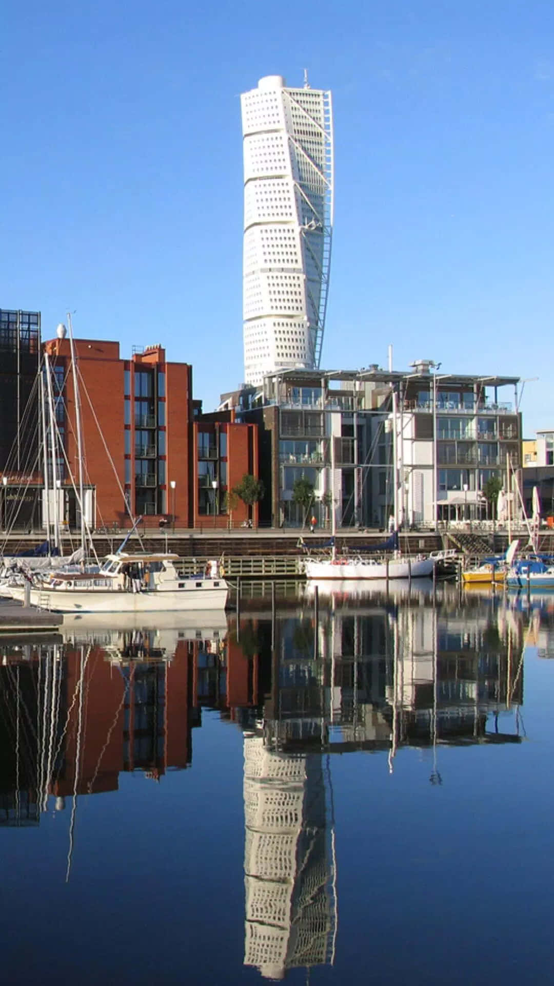 扭曲摩天大樓和港口建築倒映在平靜的水面上，伴有帆船。