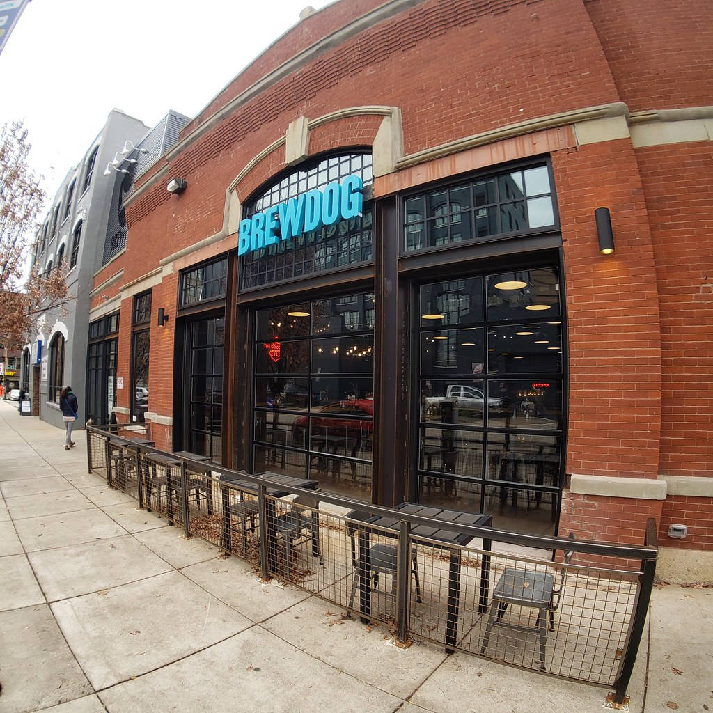 辛辛那提 BrewDog 分店熱鬧景象 壁紙 — 紅磚 BrewDog 啤酒廠，設有大窗戶和戶外座位，位於鋪滿落葉的行人路上。