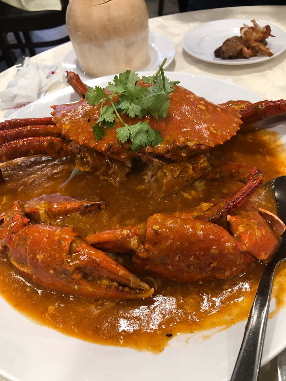 辣椒蟹料理 壁紙 — 一隻完整的蒸蟹，配上濃郁的橙醬，飾以新鮮芫荽，放在白色碟子上，在餐廳環境中。