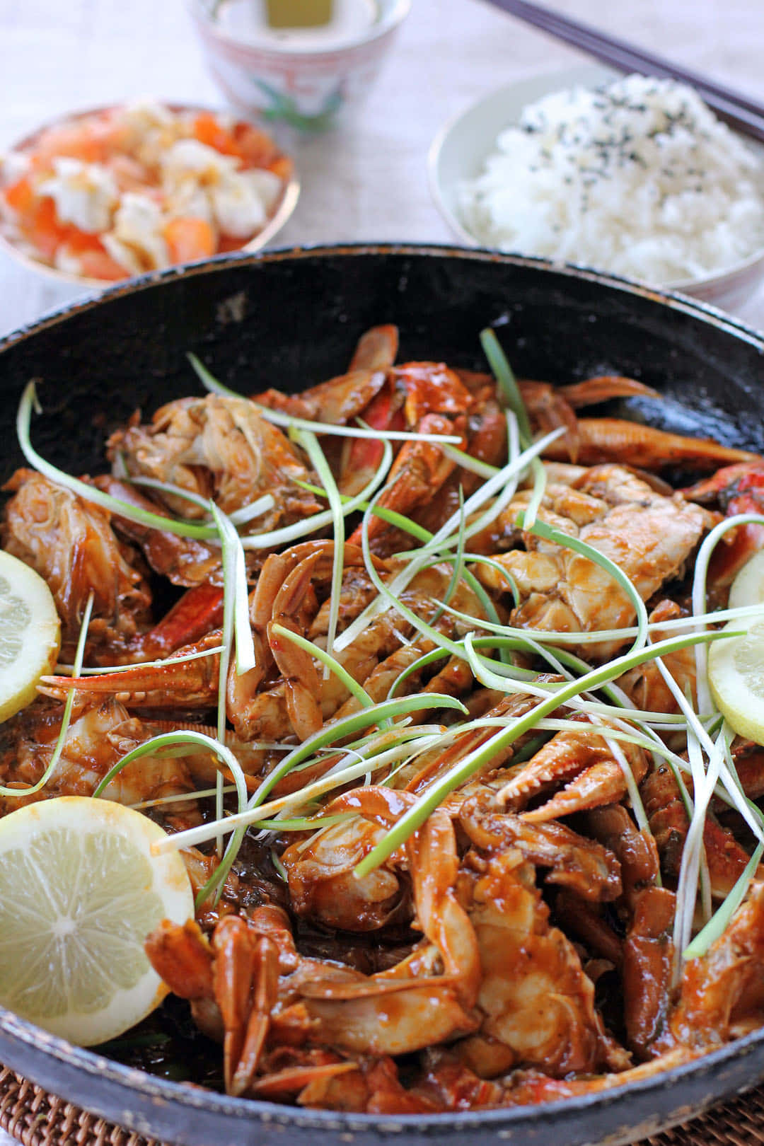 辣椒蟹配檸檬片 壁紙 — 一鍋滋滋作響的辣蟹，配上檸檬片和青蔥，旁邊有米飯和小菜。