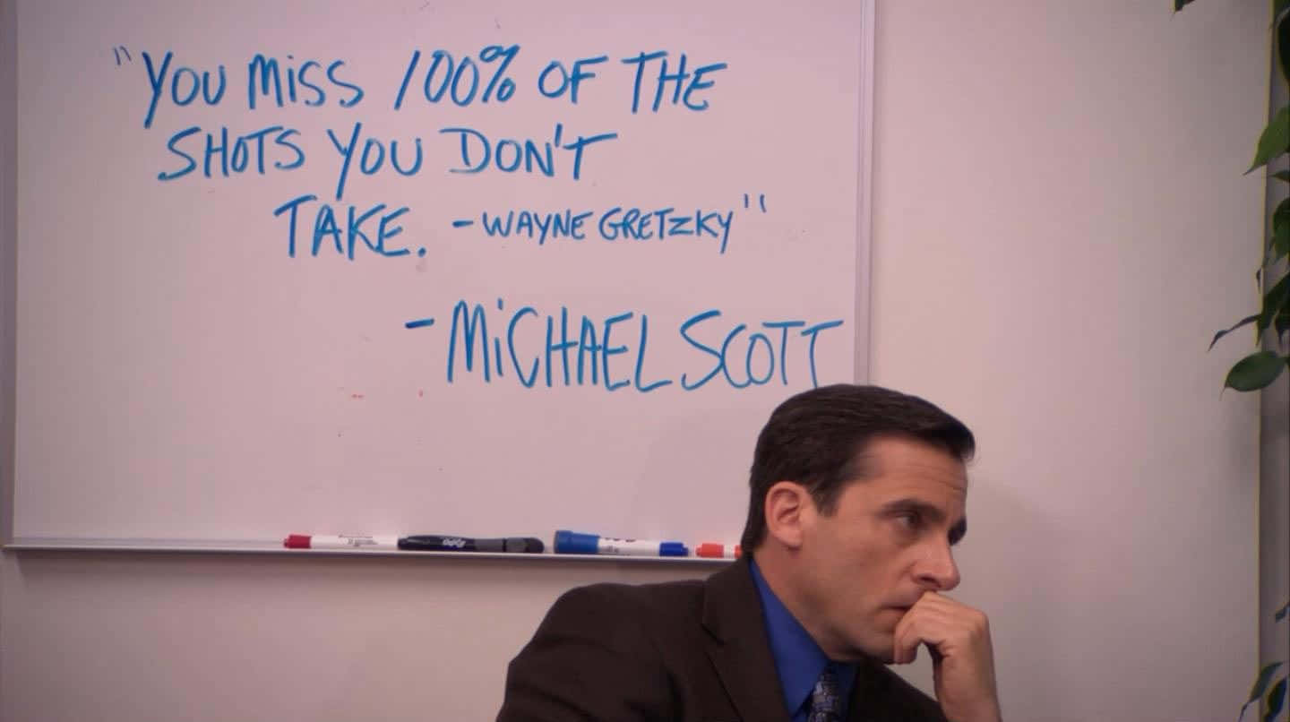 Michael Scott 在辦公室，身後白板上有名言。